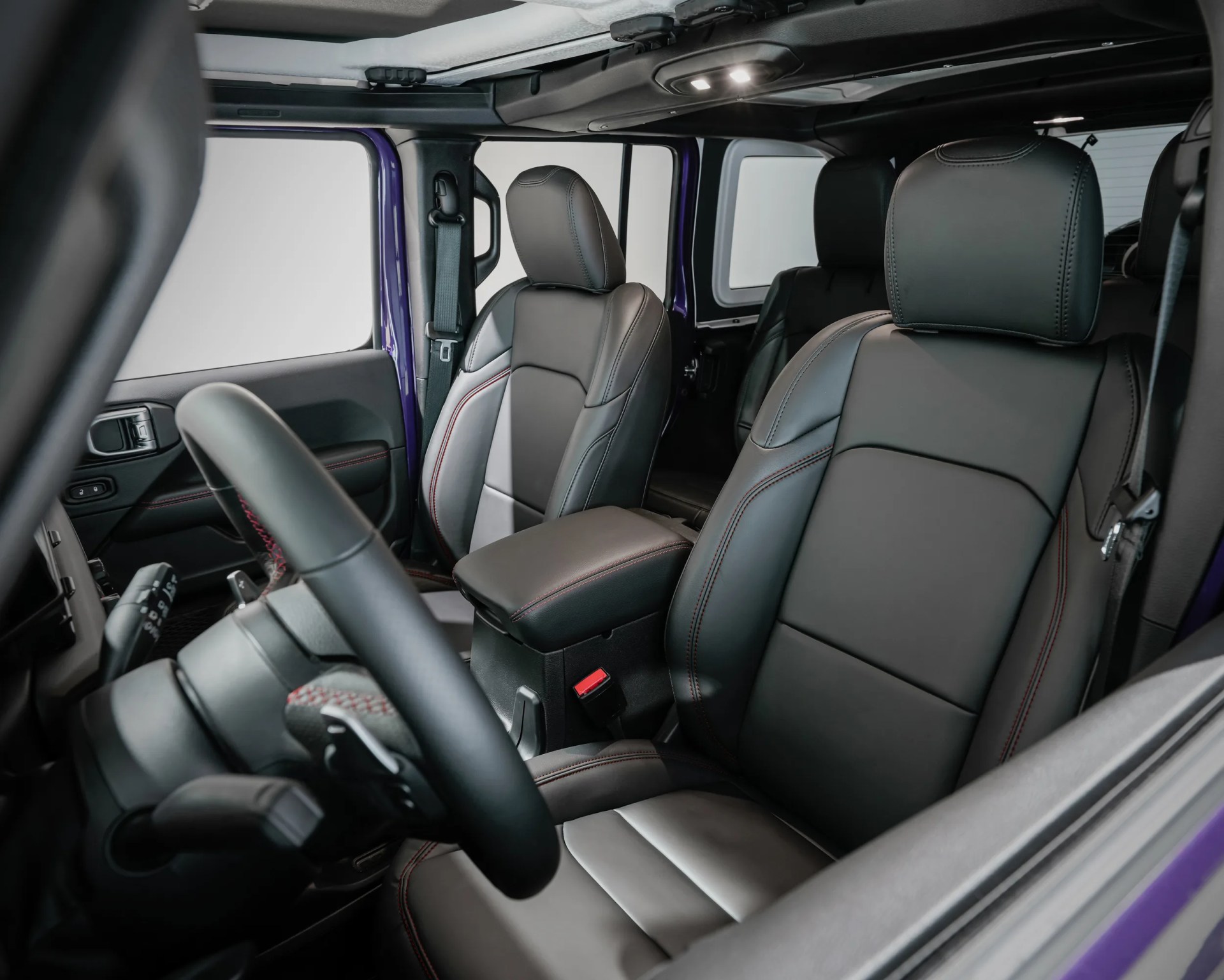 Black leather front seats with red stitching and a center armrest inside a purple vehicle.