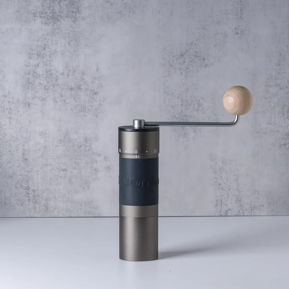 Matte black and silver manual coffee grinder with a wooden handle knob on a gray surface and textured gray background.