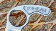 Close-up of a silver metal tool handle with "KA-BAR" engraved, resting on rusty metal branches.