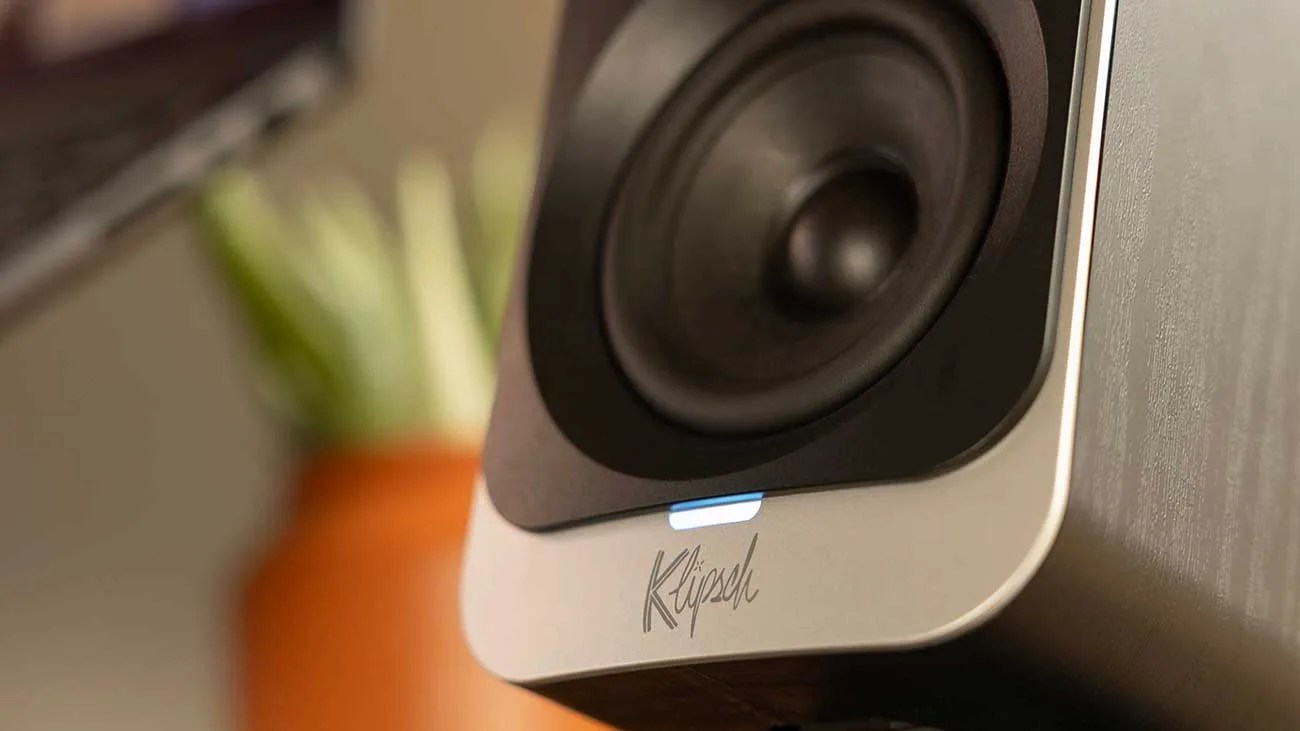 Close-up of a Klipsch speaker driver with a glowing blue indicator light on a wooden surface.