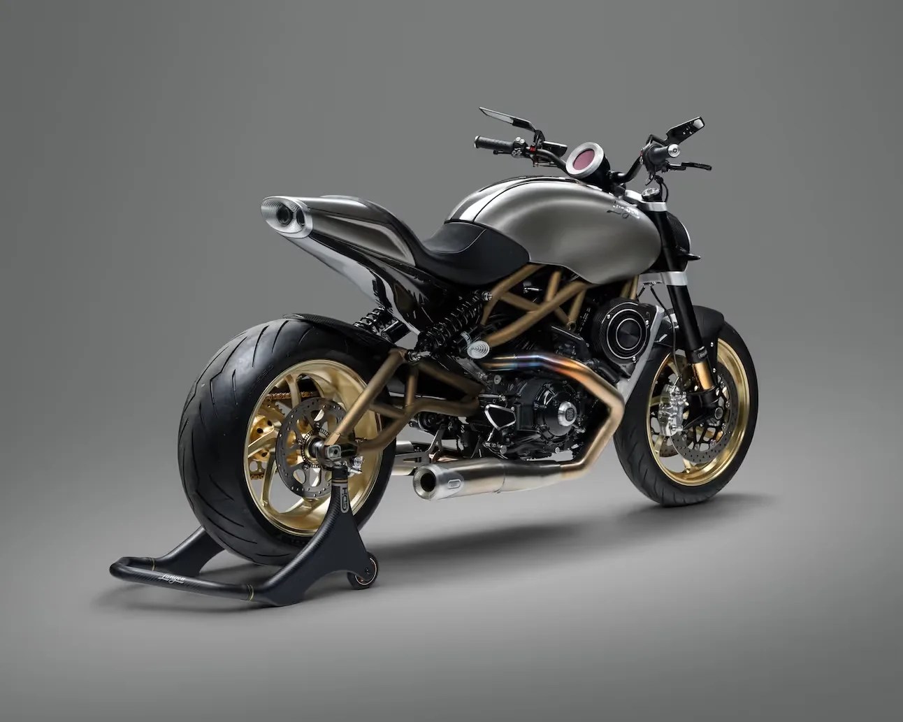 Silver and black motorcycle with gold frame and wheels on a black rear stand against a gray background.