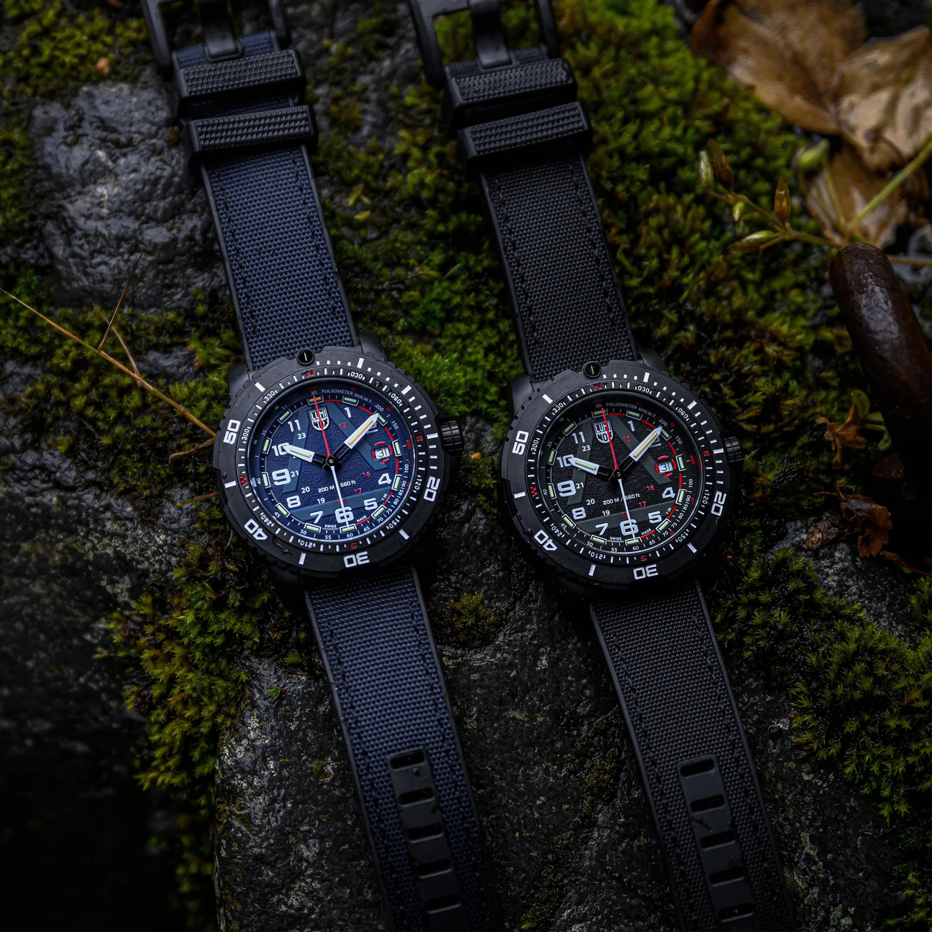 Two black rugged wristwatches with textured straps, one navy blue and one black, placed on mossy rocks.