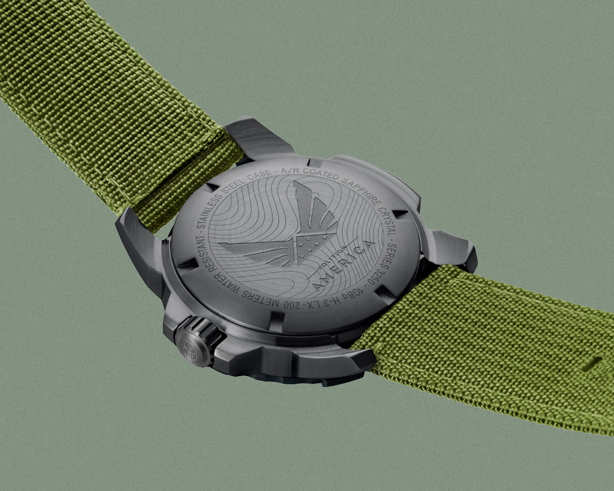 Black stainless steel watch case back with engraved design and olive green fabric strap.