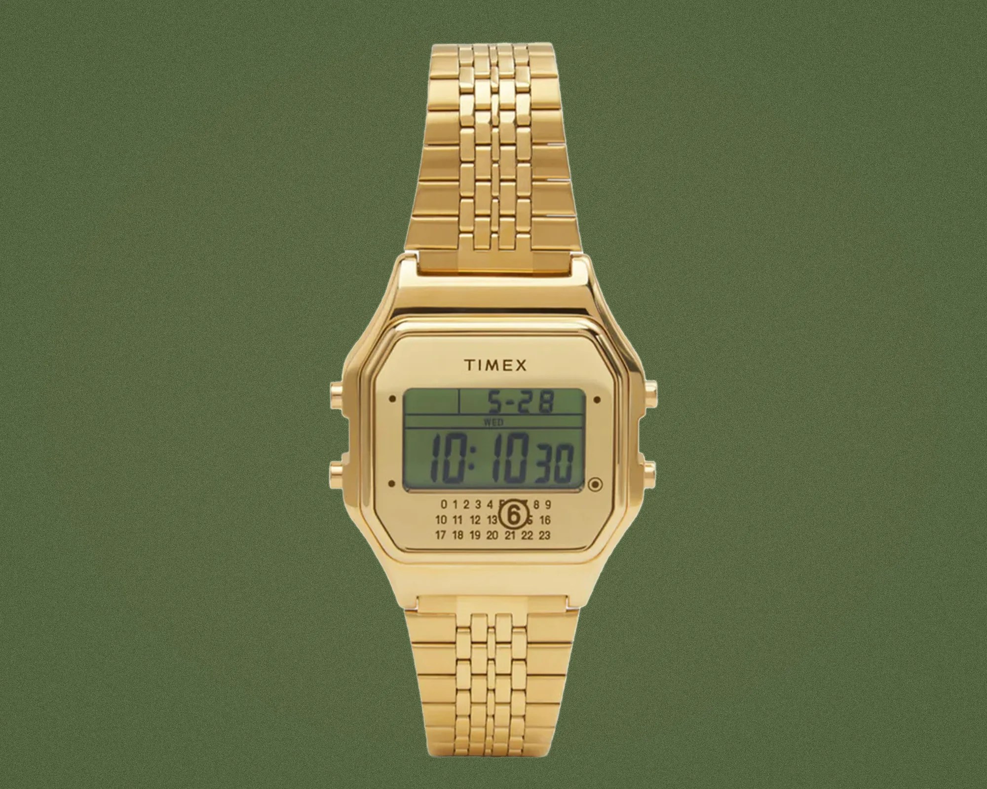 Gold-tone Timex digital watch with rectangular face and linked metal bracelet on green background.