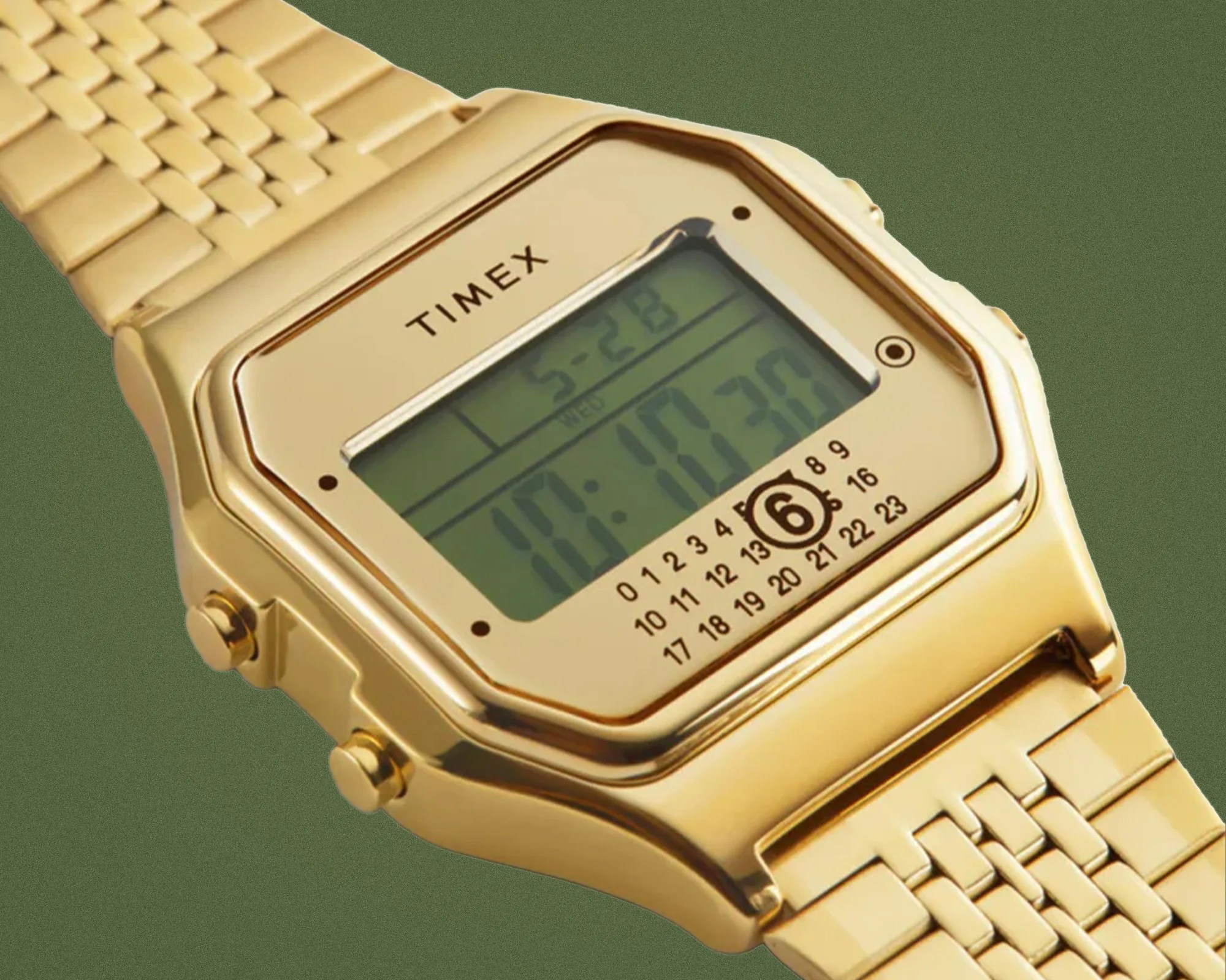 Gold-toned Timex digital watch with rectangular face and linked metal band on green background.