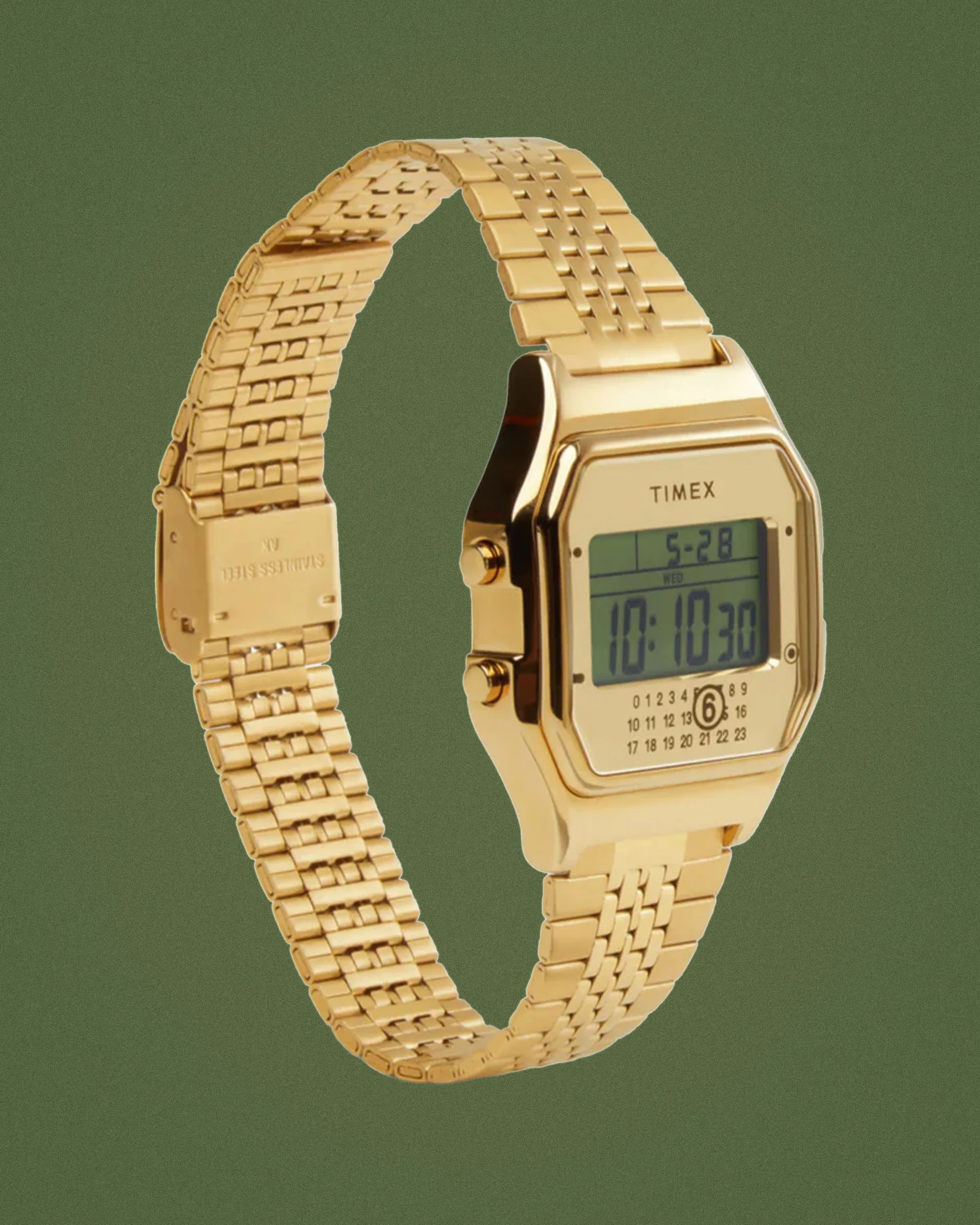Gold-tone Timex digital watch with rectangular face and metal link bracelet on green background.