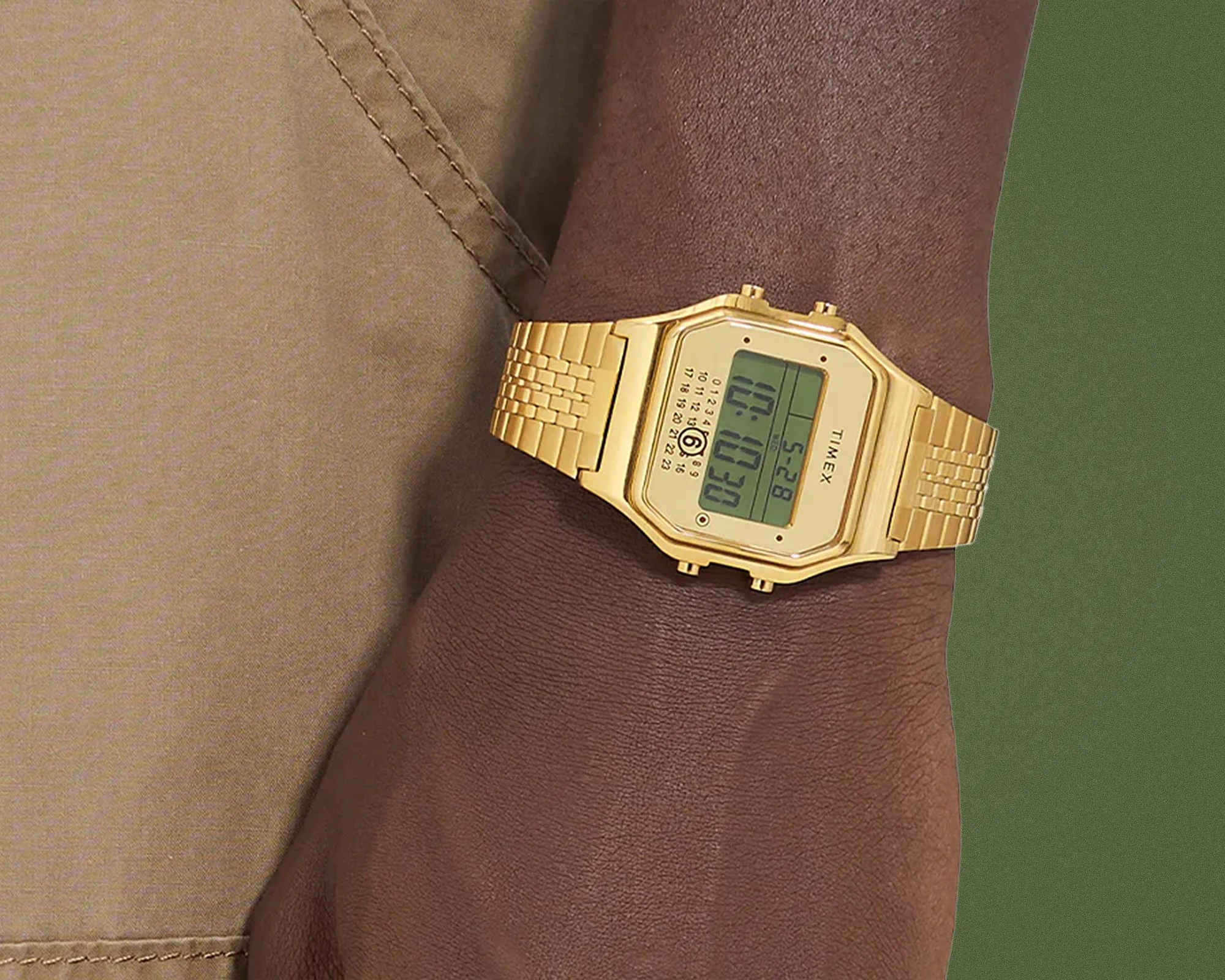 Gold-tone digital Timex watch with a rectangular face and metal link bracelet on a wrist.