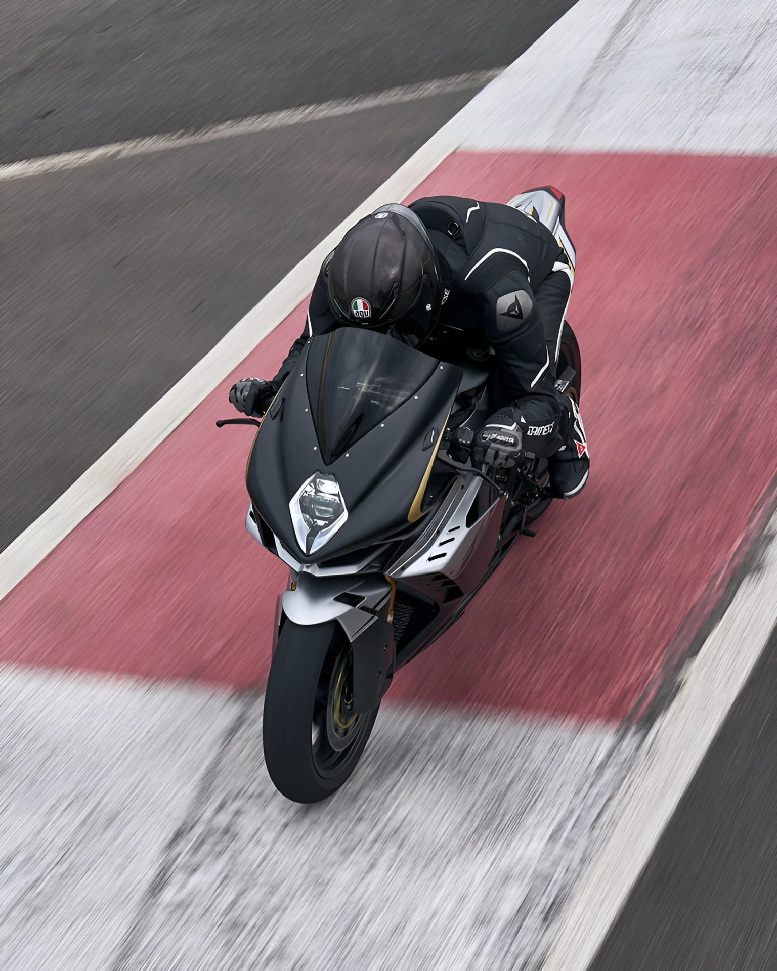 Black and silver sport motorcycle with rider in black gear on a racetrack with red and white markings.