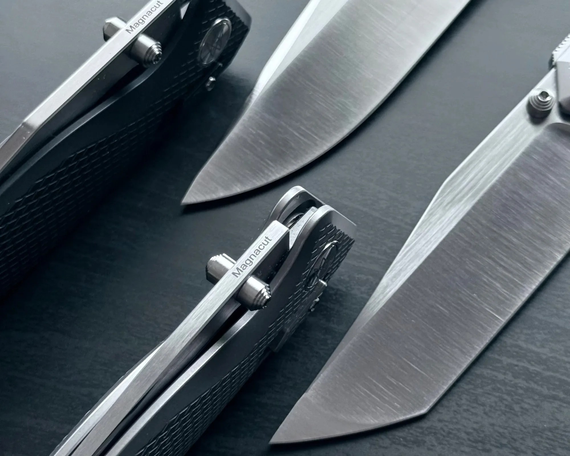 Two Magnacut folding knives with textured handles and partially open blades on a dark surface.