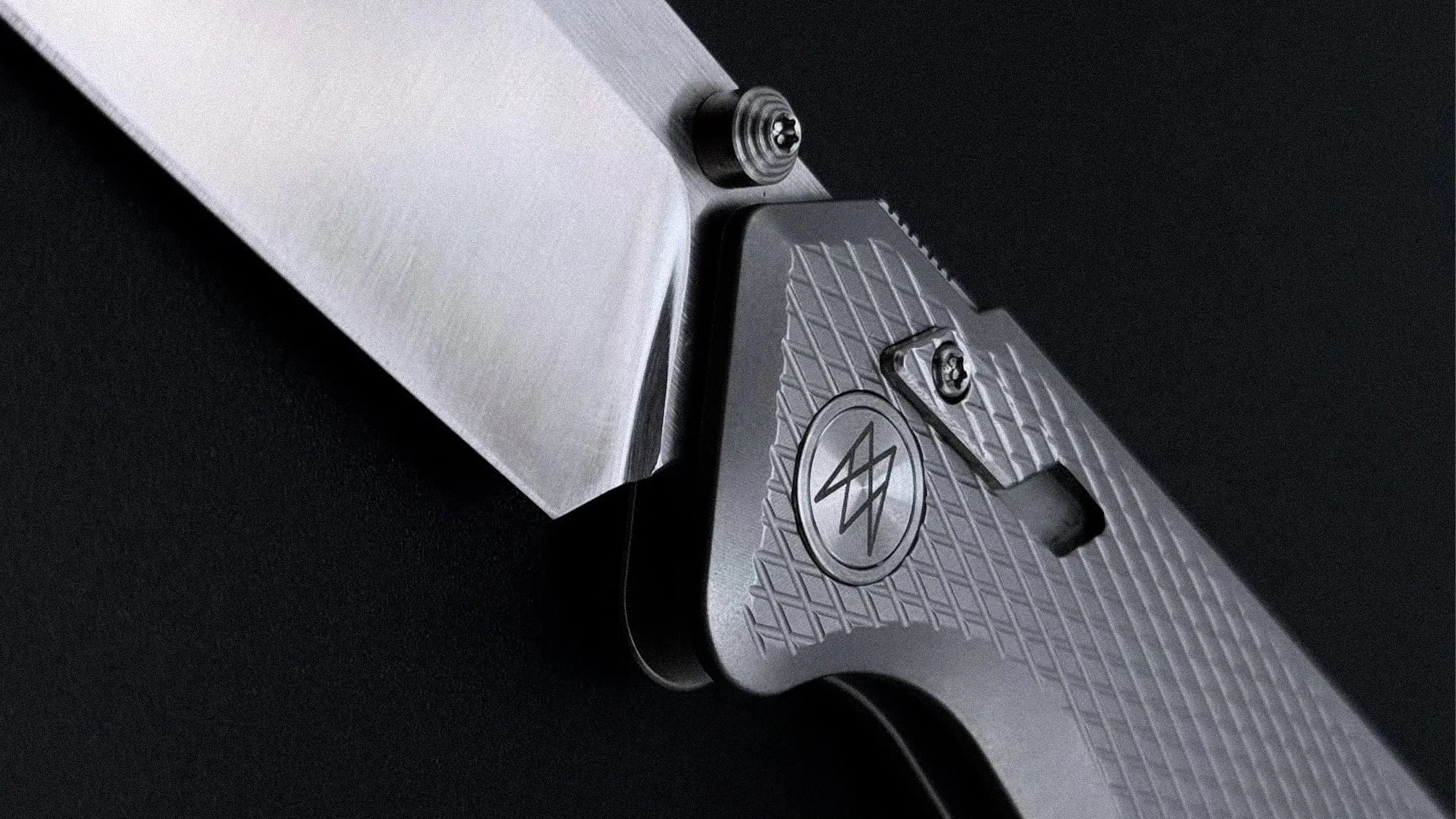 Close-up of a folding knife with a textured gray handle and a partially open silver blade against a black background.