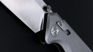 Close-up of a folding knife with a textured gray handle and a partially open silver blade against a black background.