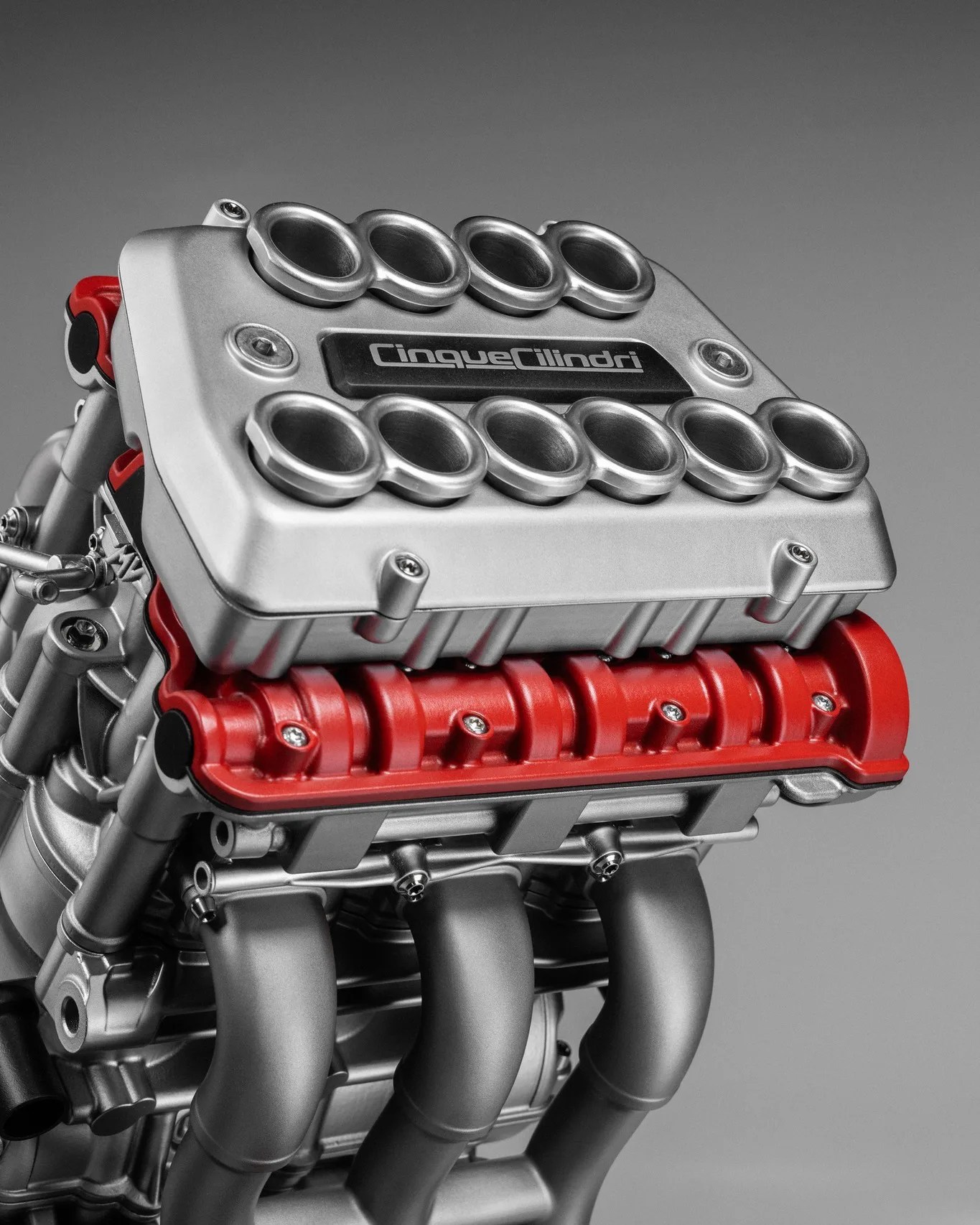 Close-up of a silver and red Cinque Cilindri engine with visible intake trumpets and exhaust pipes.
