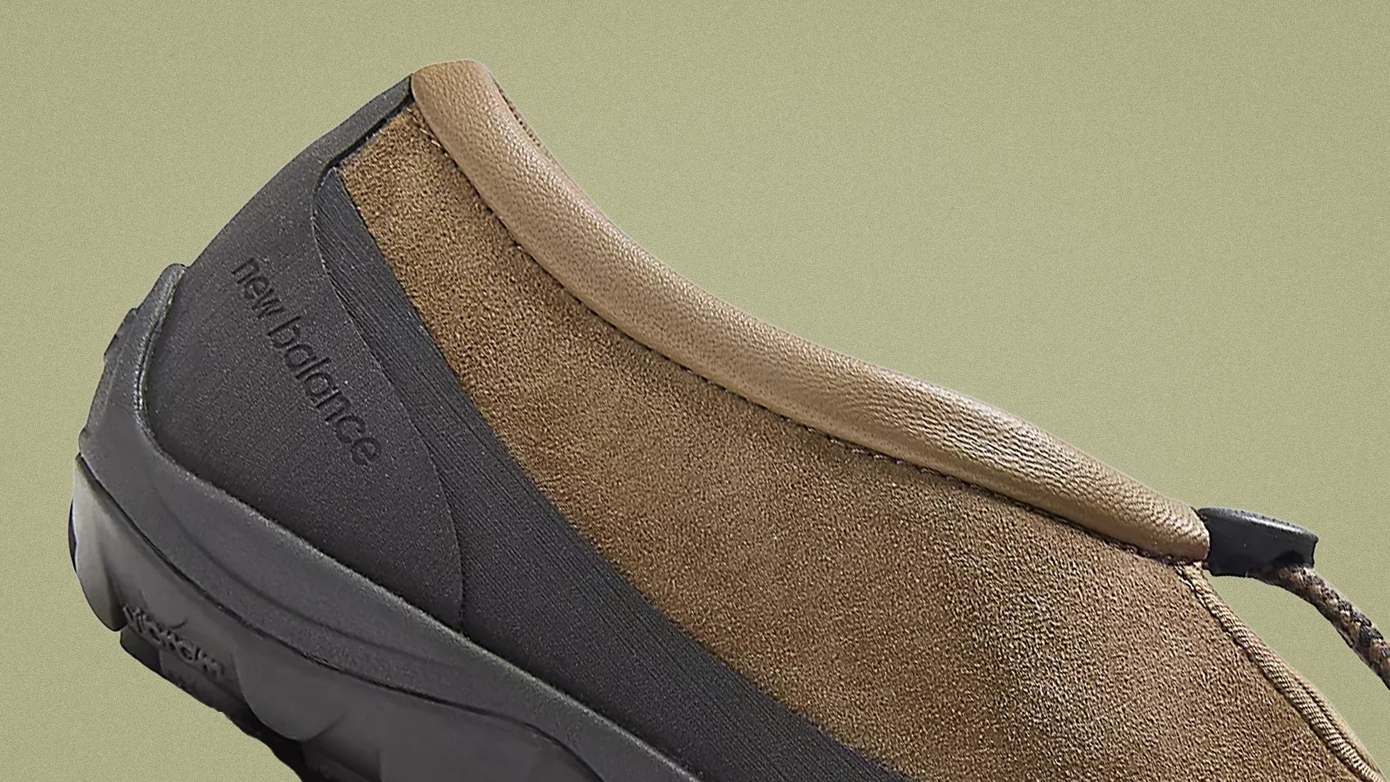 Brown suede New Balance shoe with black sole and collar trim, close-up side view.