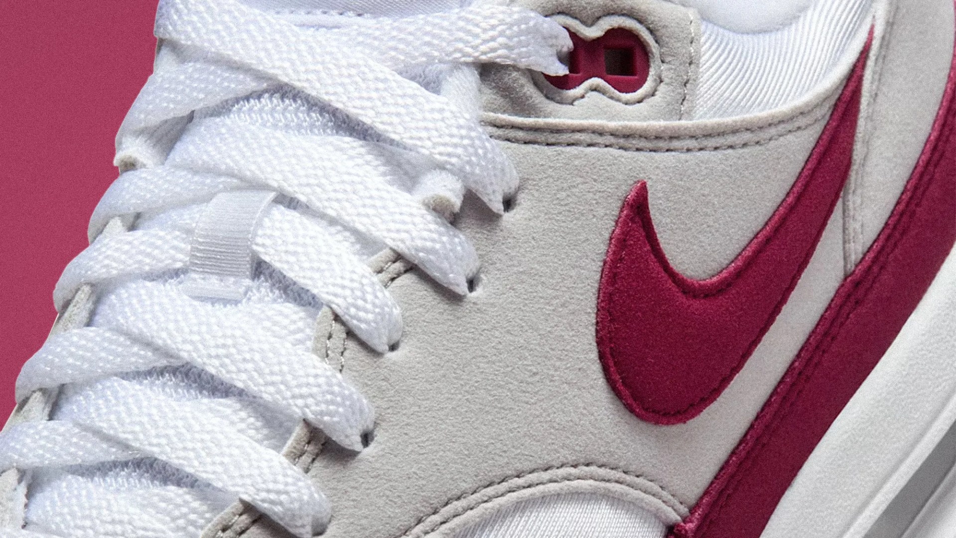 Close-up of a white sneaker with white laces and a red Nike swoosh logo on a light gray suede panel.