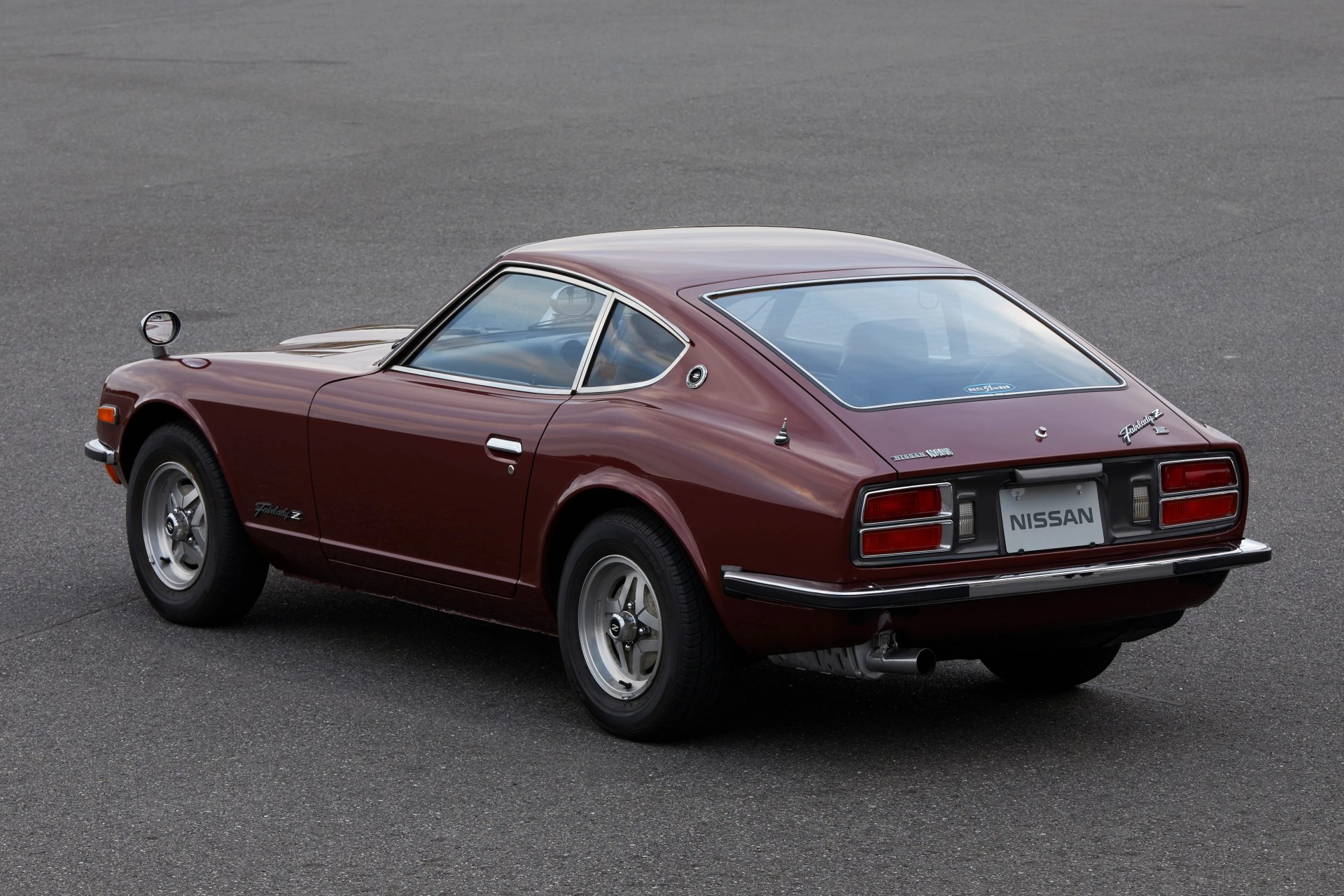 Maroon vintage Nissan Fairlady Z sports car parked on asphalt, rear three-quarter view.