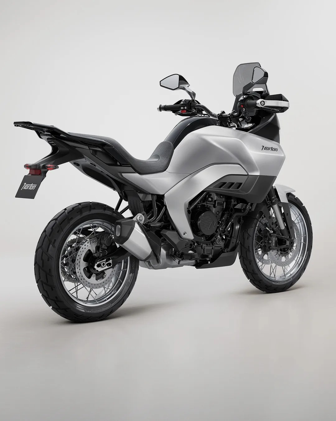 Silver and black Norton adventure motorcycle with spoked wheels and a tall windshield on a plain background.