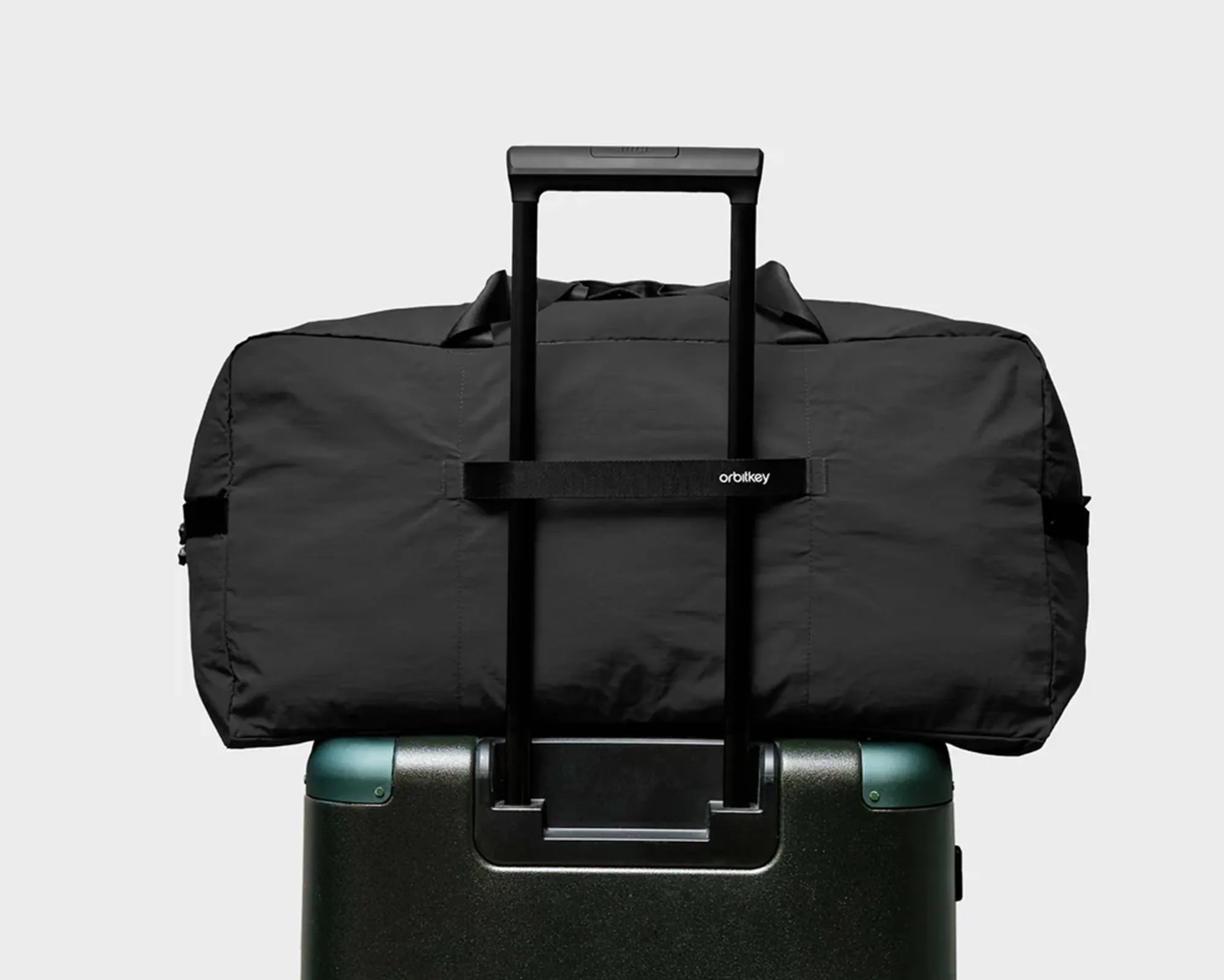 Black duffel bag secured on the handle of a dark green hard-shell suitcase.