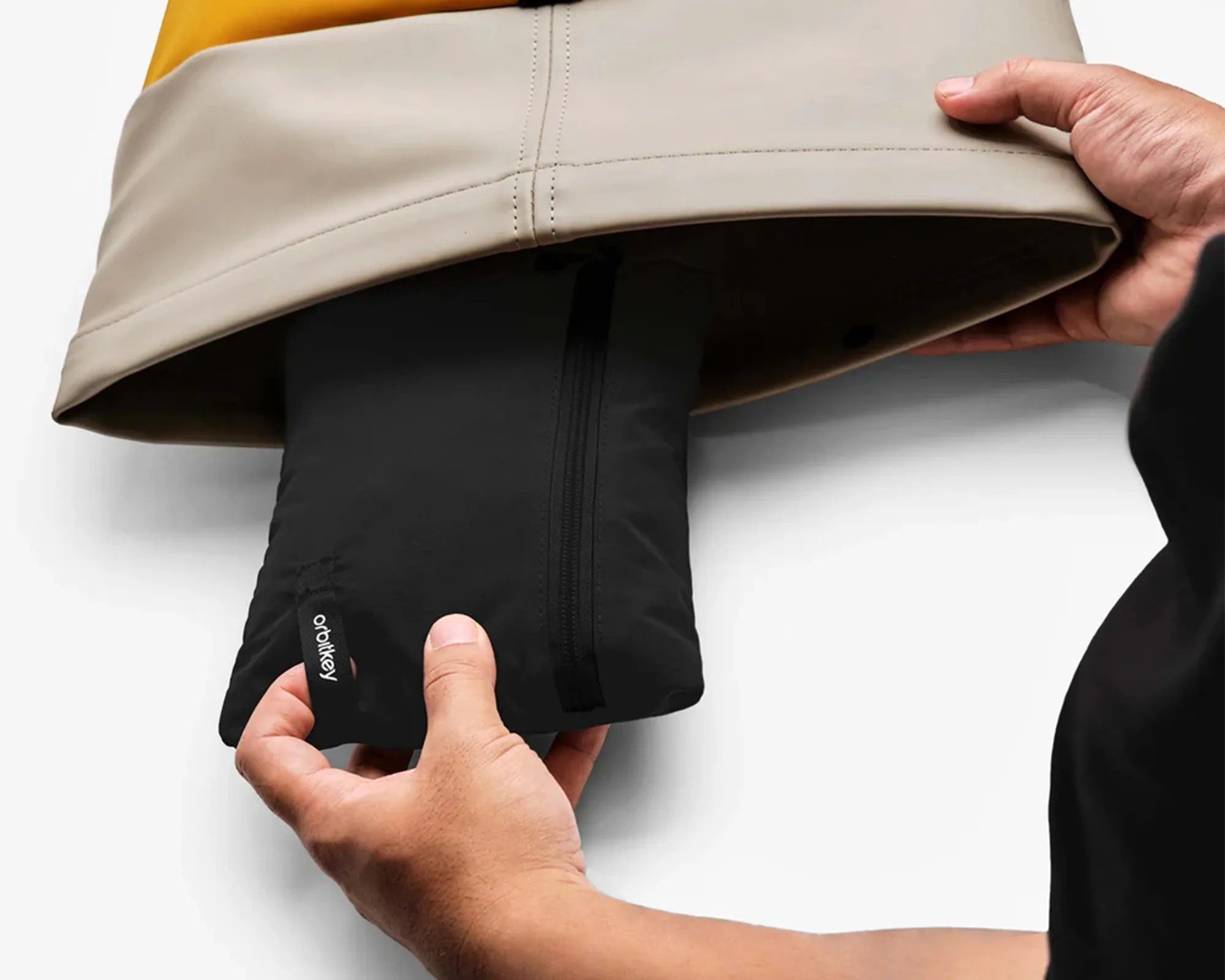 Hands holding a black folded jacket with a visible "orbitkey" tag being pulled out from a beige garment.