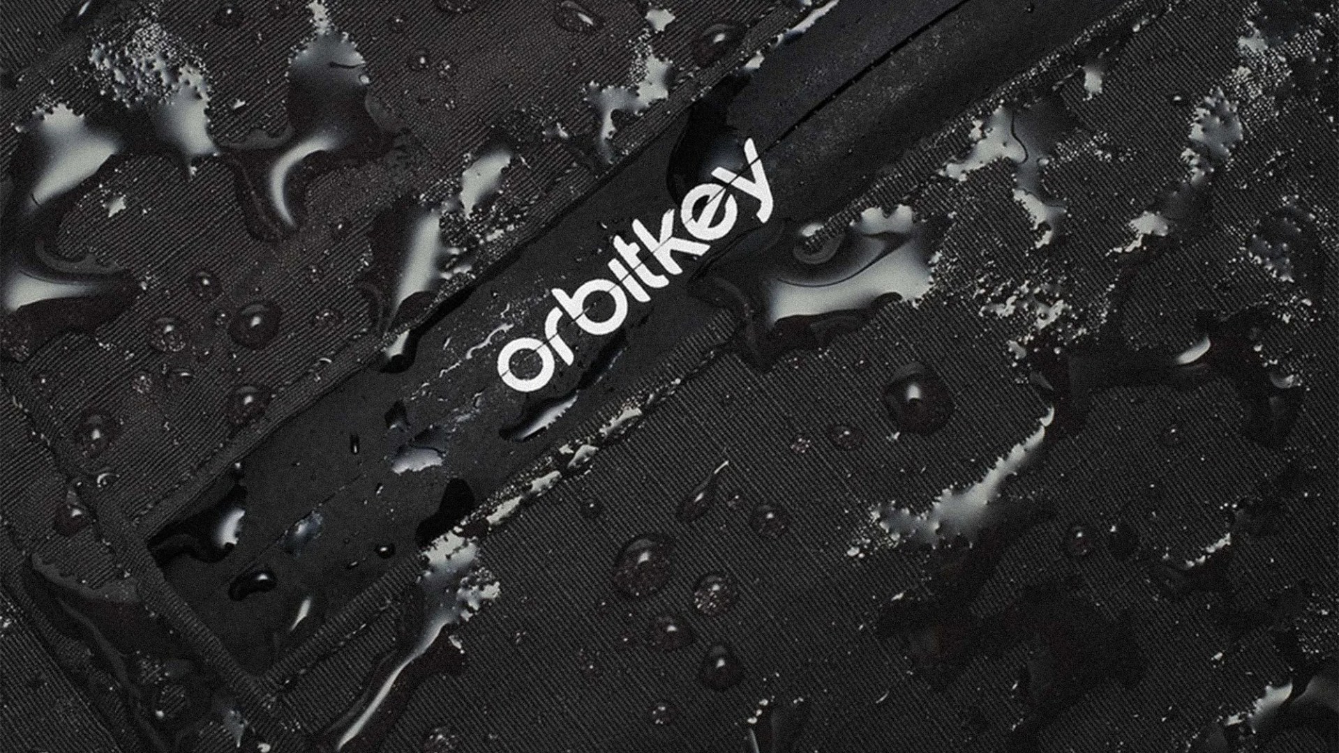 Close-up of black fabric with water droplets and a white "orbitkey" logo on a waterproof zipper.