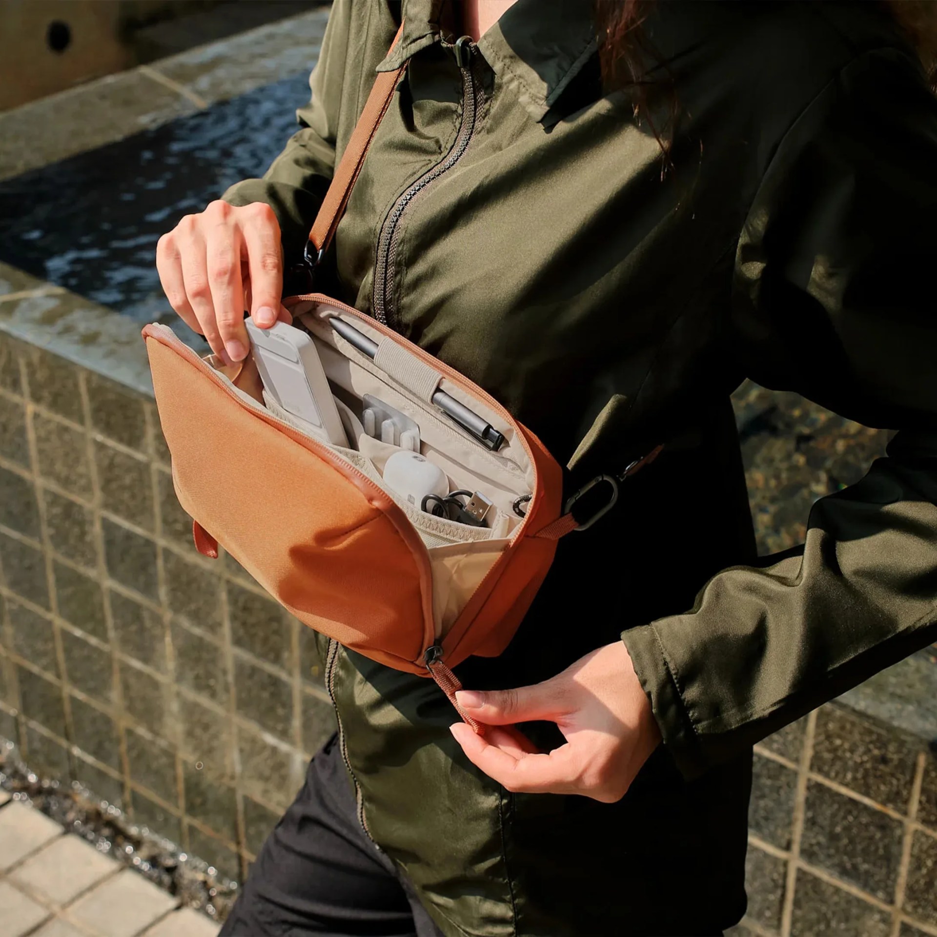 Brown crossbody organizer bag with multiple compartments holding a phone, pen, and charging cables.