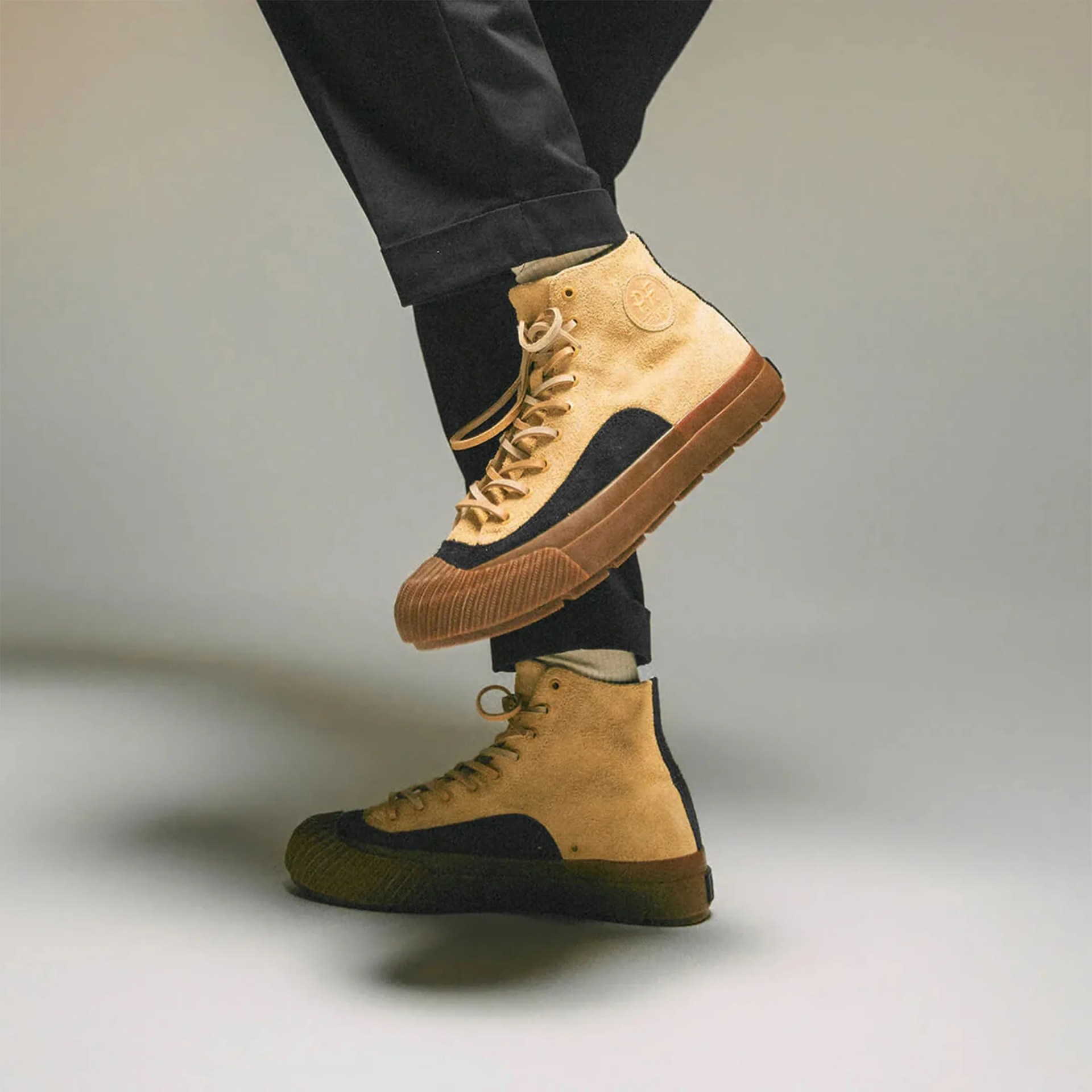 Tan and black high-top sneakers with brown rubber soles worn with black pants.