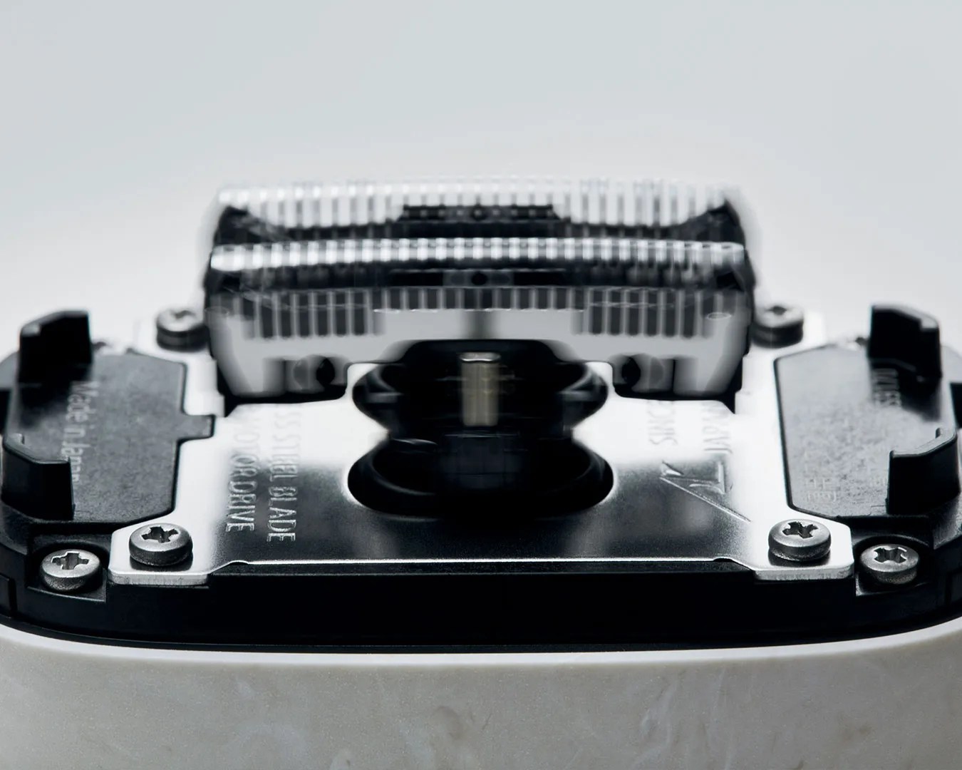 Close-up of a silver and black electric razor blade head with screws and plastic components.
