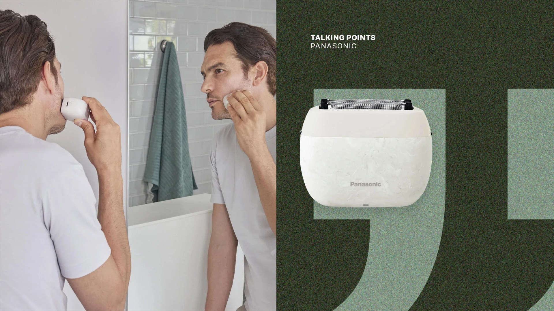 Man using a white Panasonic electric shaver in front of a bathroom mirror with a green towel hanging.