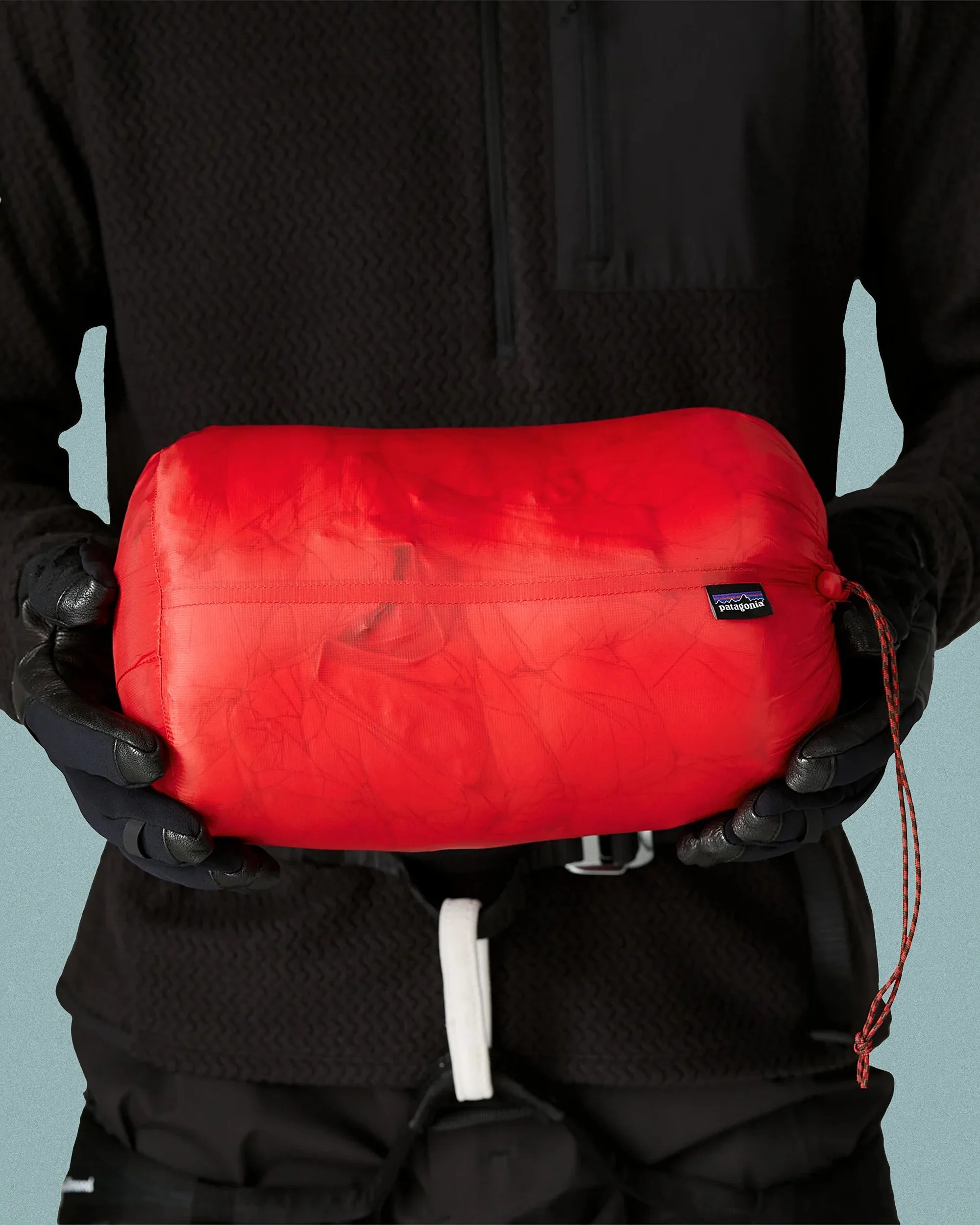Red Patagonia stuff sack held by a person wearing black gloves and black clothing.