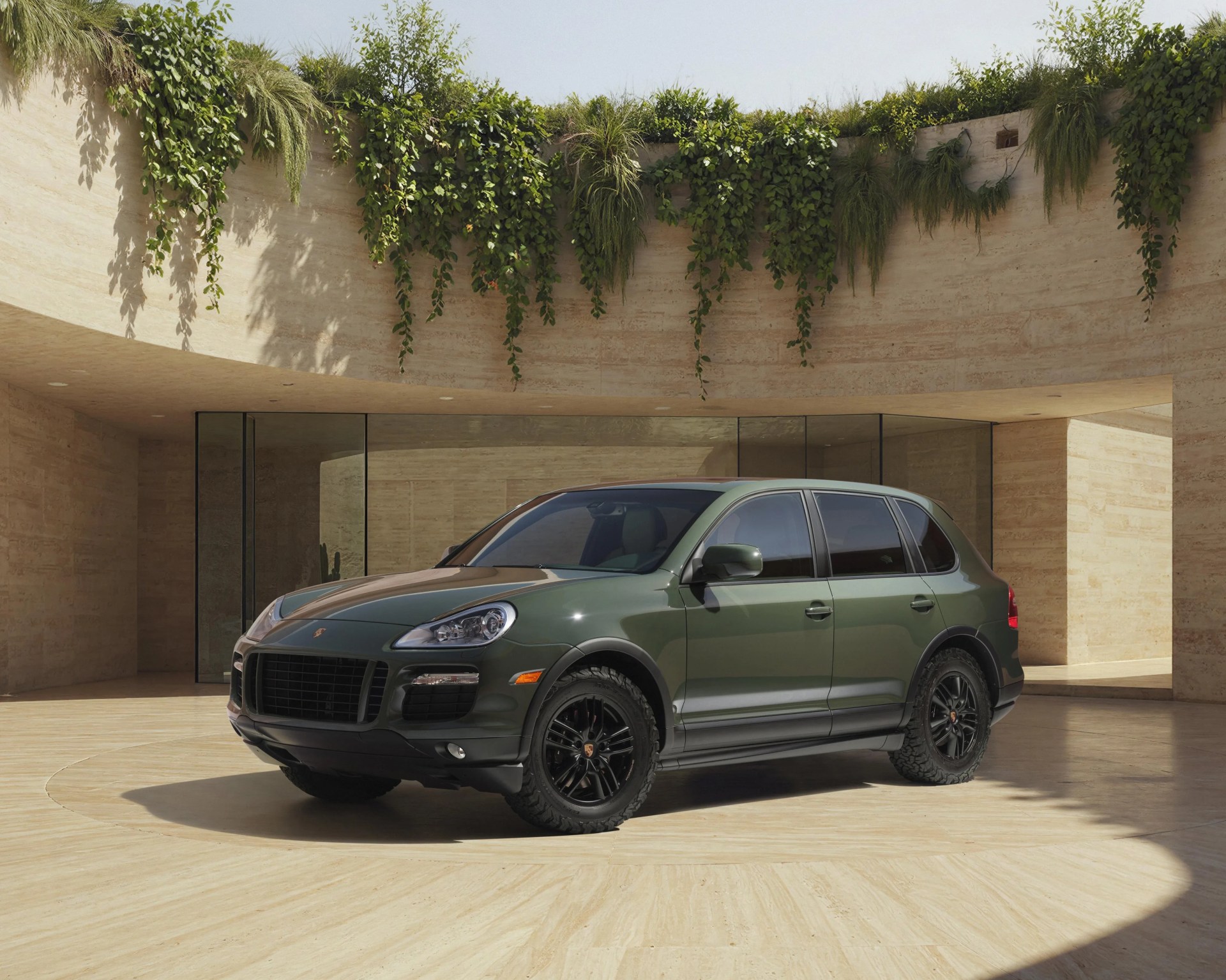 Dark green Porsche SUV with black wheels parked in a circular beige stone courtyard with hanging greenery.