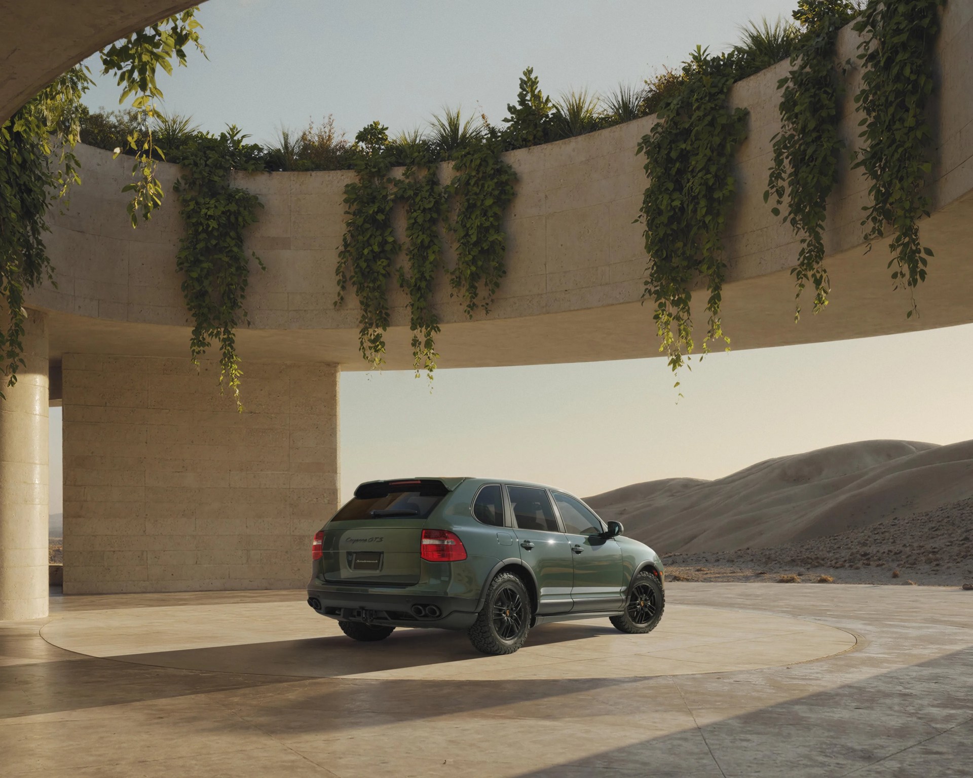 Green Porsche Cayenne GTS SUV parked under a curved concrete structure with hanging plants and desert hills in the background.