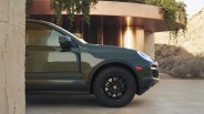 Dark green Porsche SUV front side with black wheels parked near a modern building with hanging plants.
