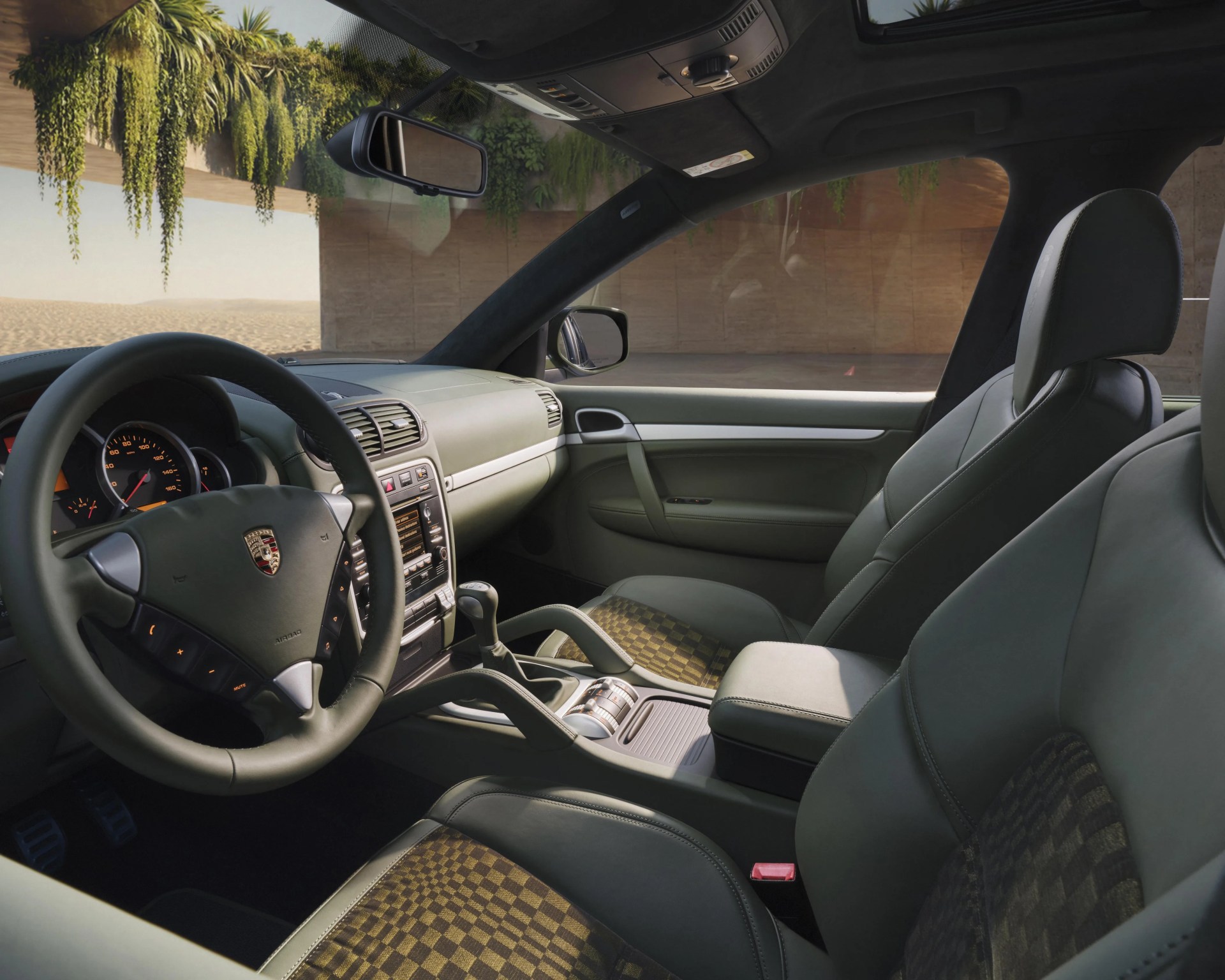 Interior of a Porsche car featuring black leather seats with checkered fabric inserts and a black leather steering wheel with the Porsche logo.