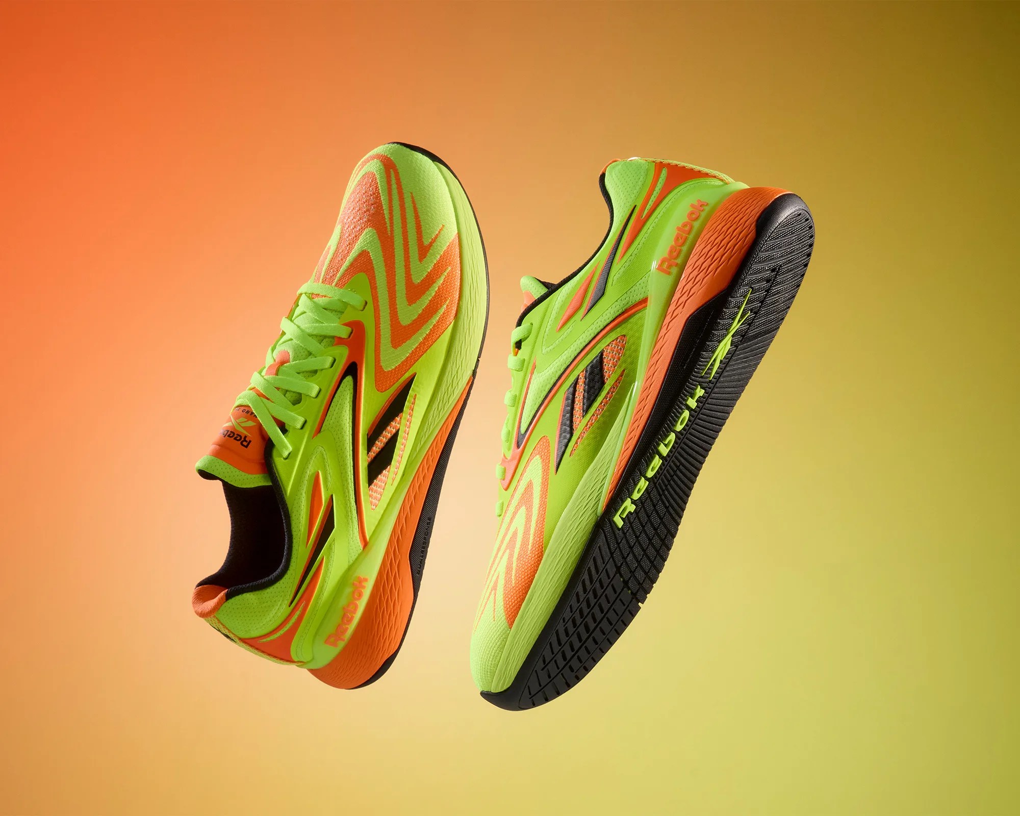 Pair of neon green and orange Reebok running shoes with black soles against an orange-yellow gradient background.
