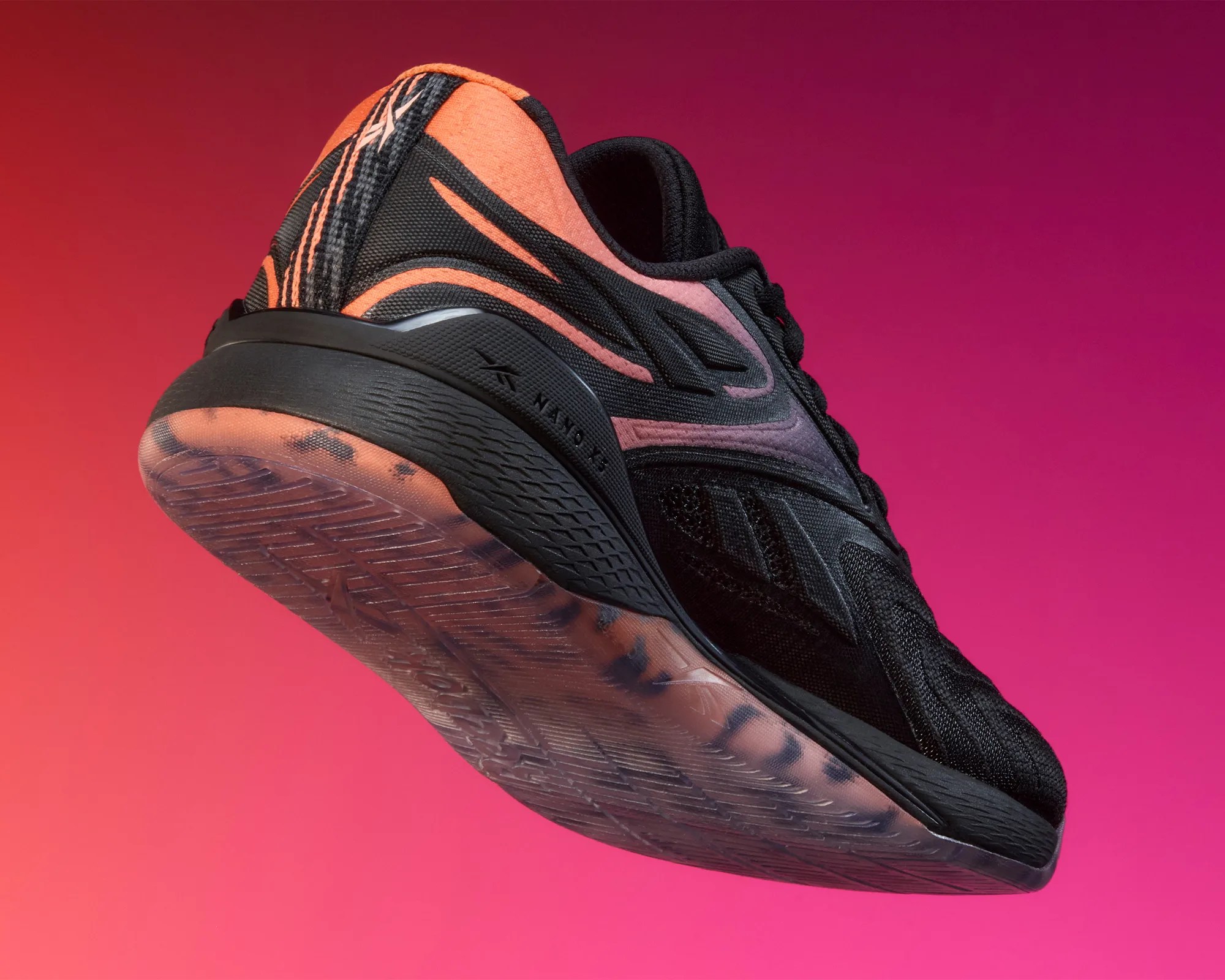Black and orange athletic shoe with textured sole and gradient upper against a pink background.