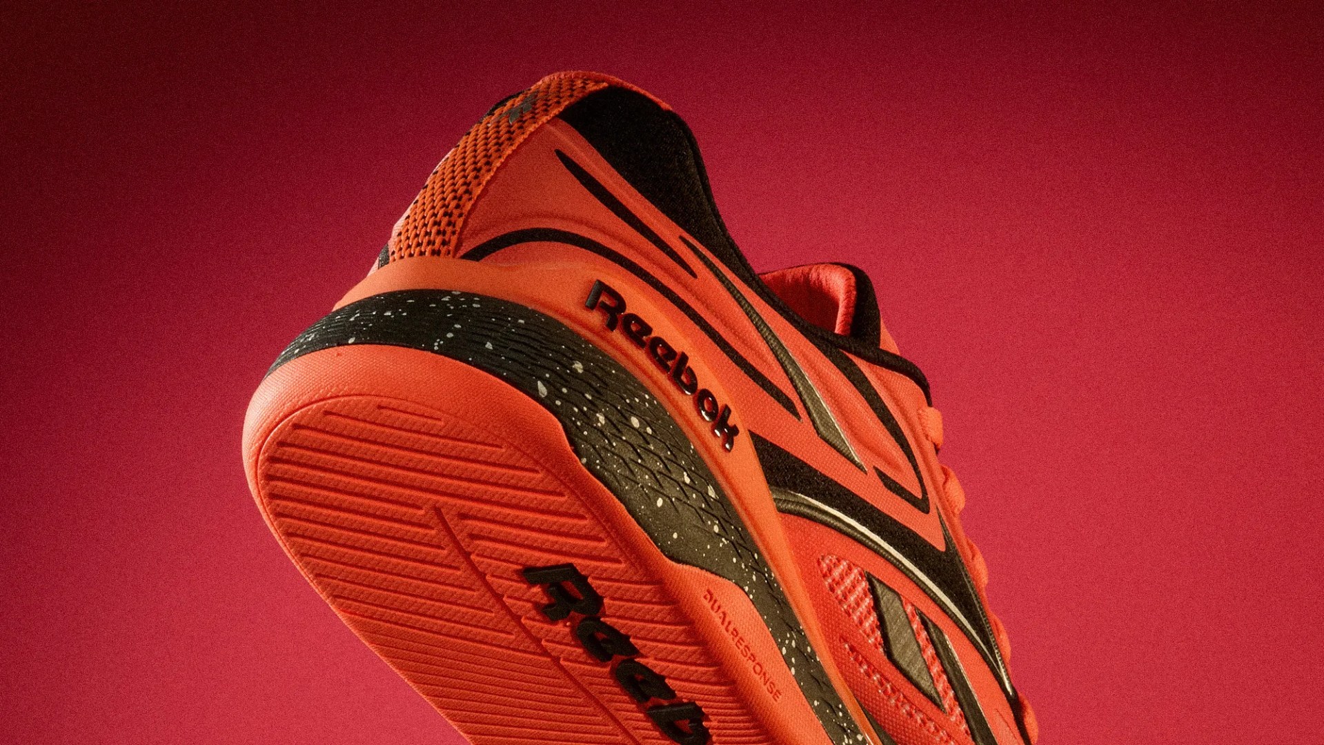 Orange and black Reebok running shoe with speckled midsole on a red background.
