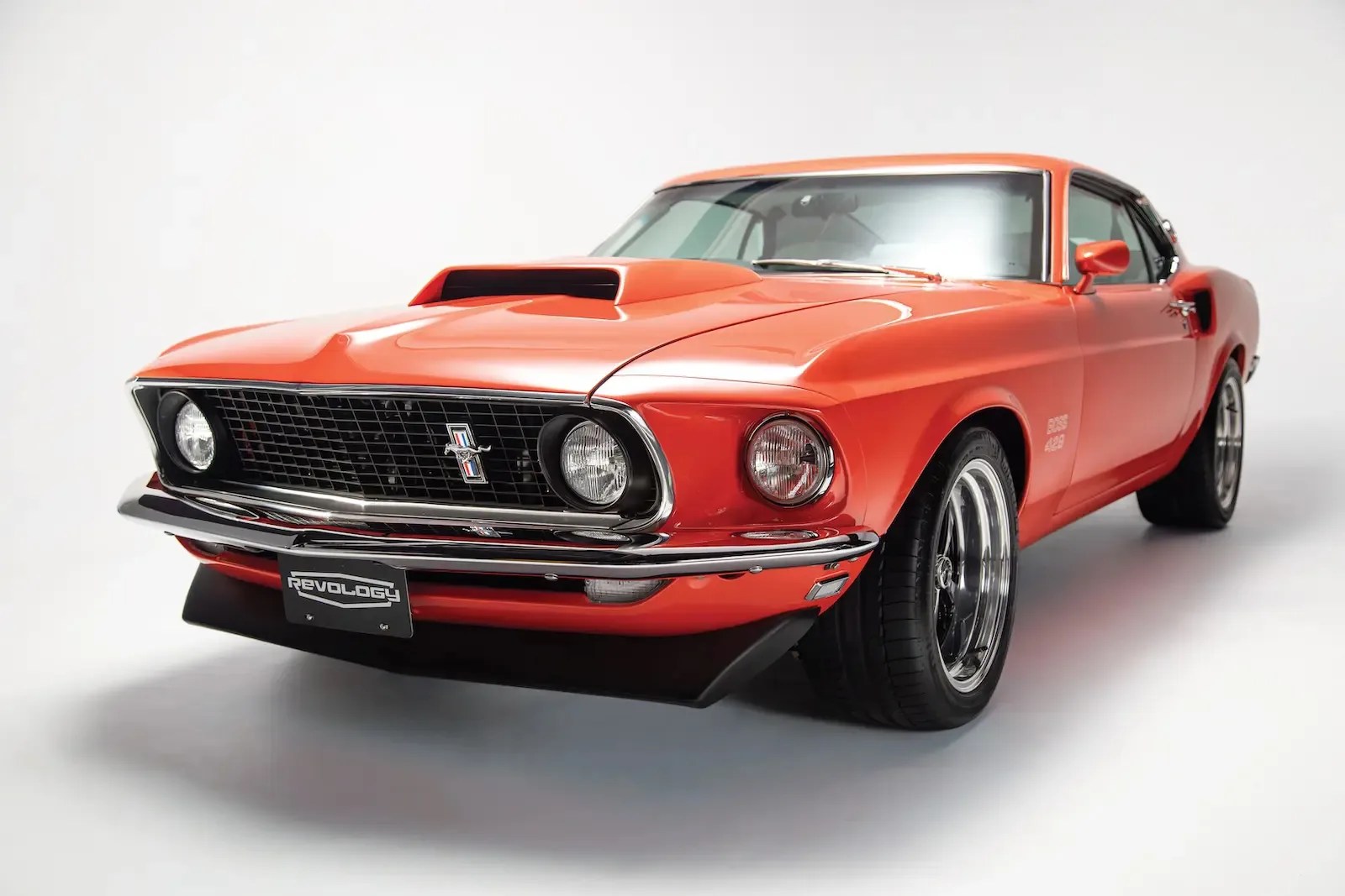Orange classic Ford Mustang Boss 429 with black grille and chrome bumper in a studio setting.