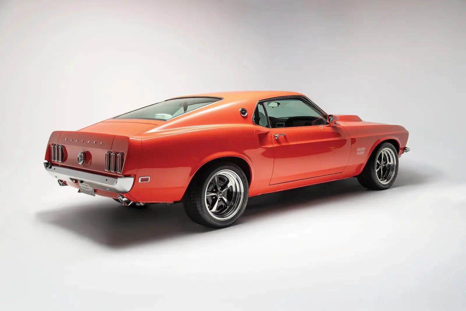 Orange 1969 Ford Mustang Boss 429 with black five-spoke wheels in a studio setting.