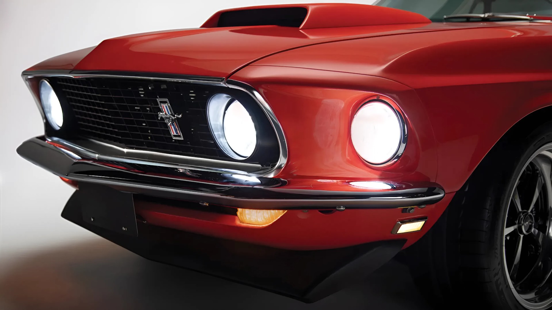 Front view of a red classic Ford Mustang with illuminated round headlights and black grille with Mustang emblem.
