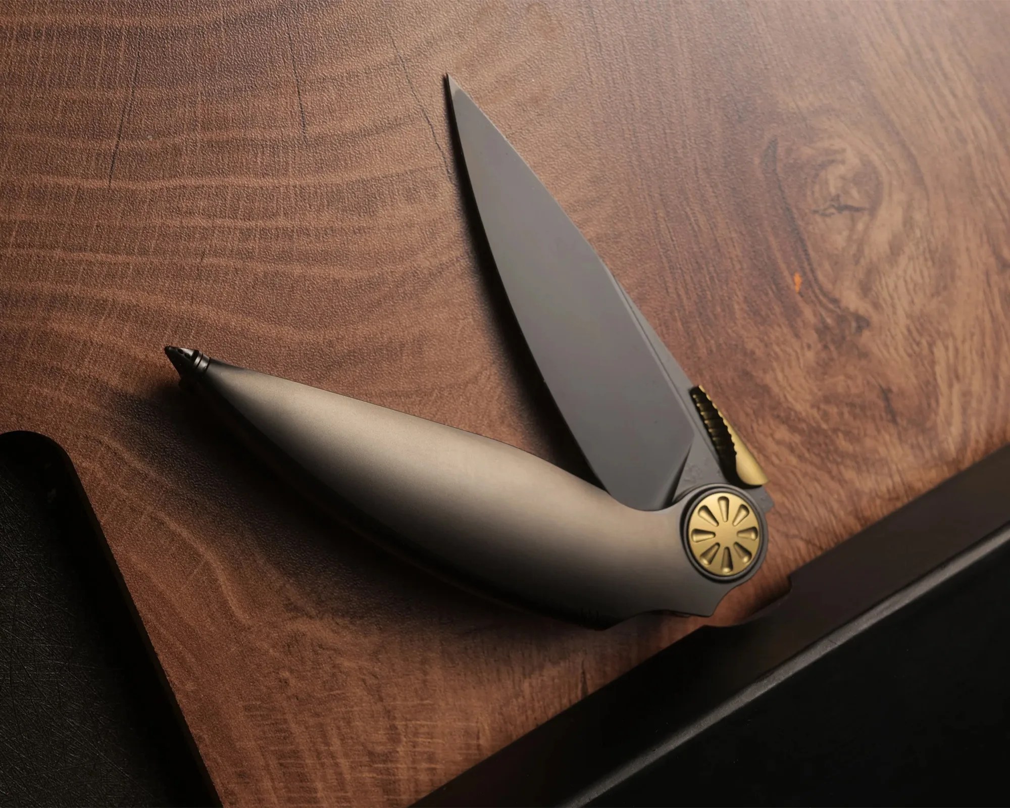 Matte gray folding knife with gold pivot and thumb stud on a wooden surface.