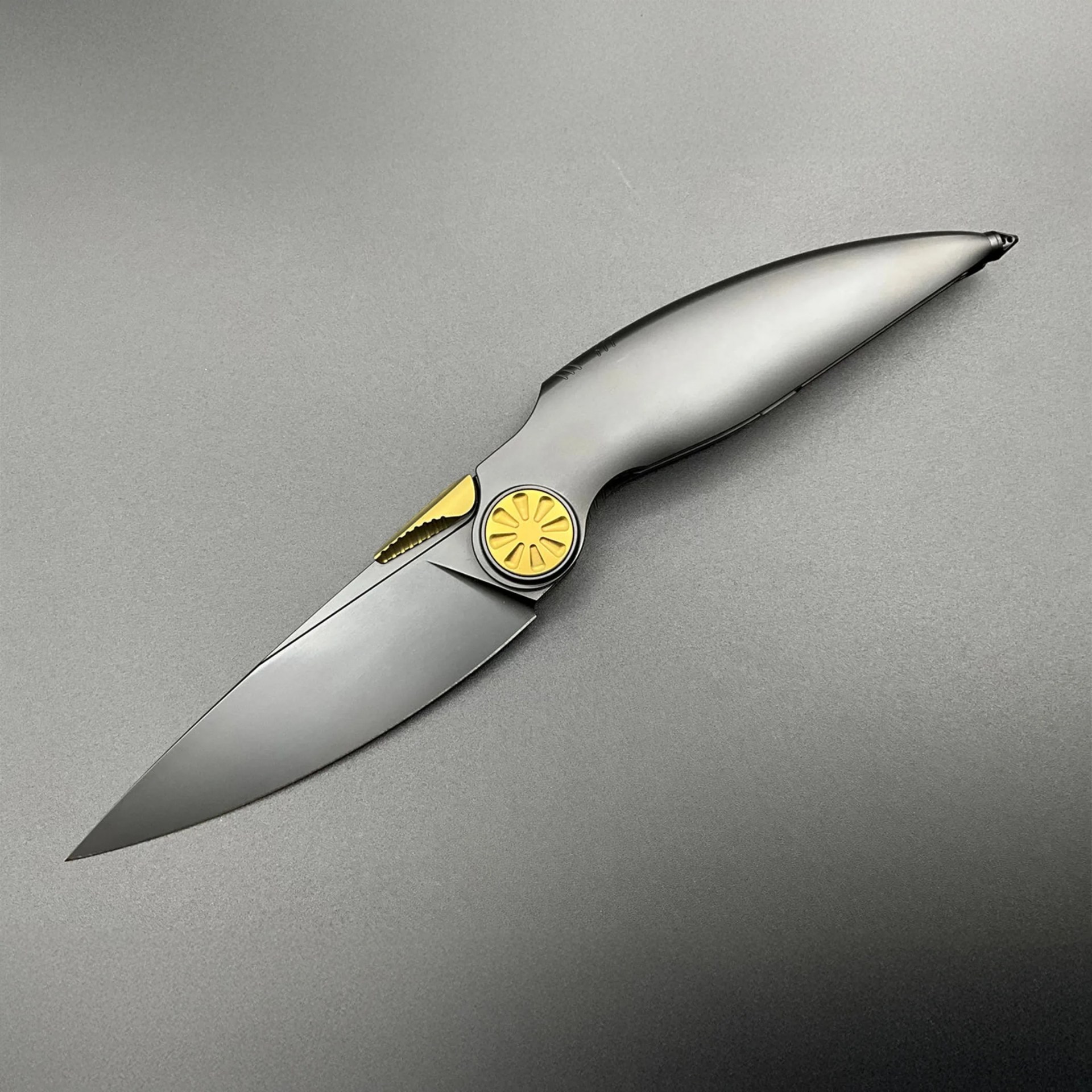 Sleek folding knife with matte silver blade and handle, featuring gold pivot and thumb stud accents.