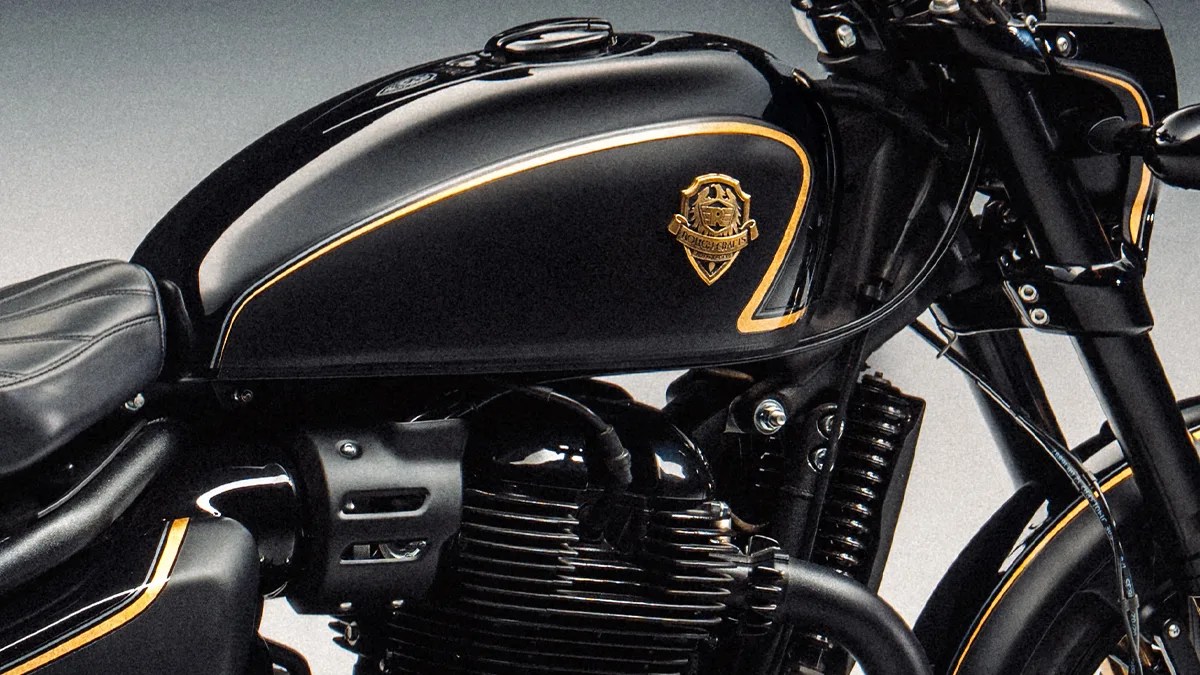 Close-up of a black motorcycle fuel tank with gold trim and emblem, showing part of the engine and front suspension.