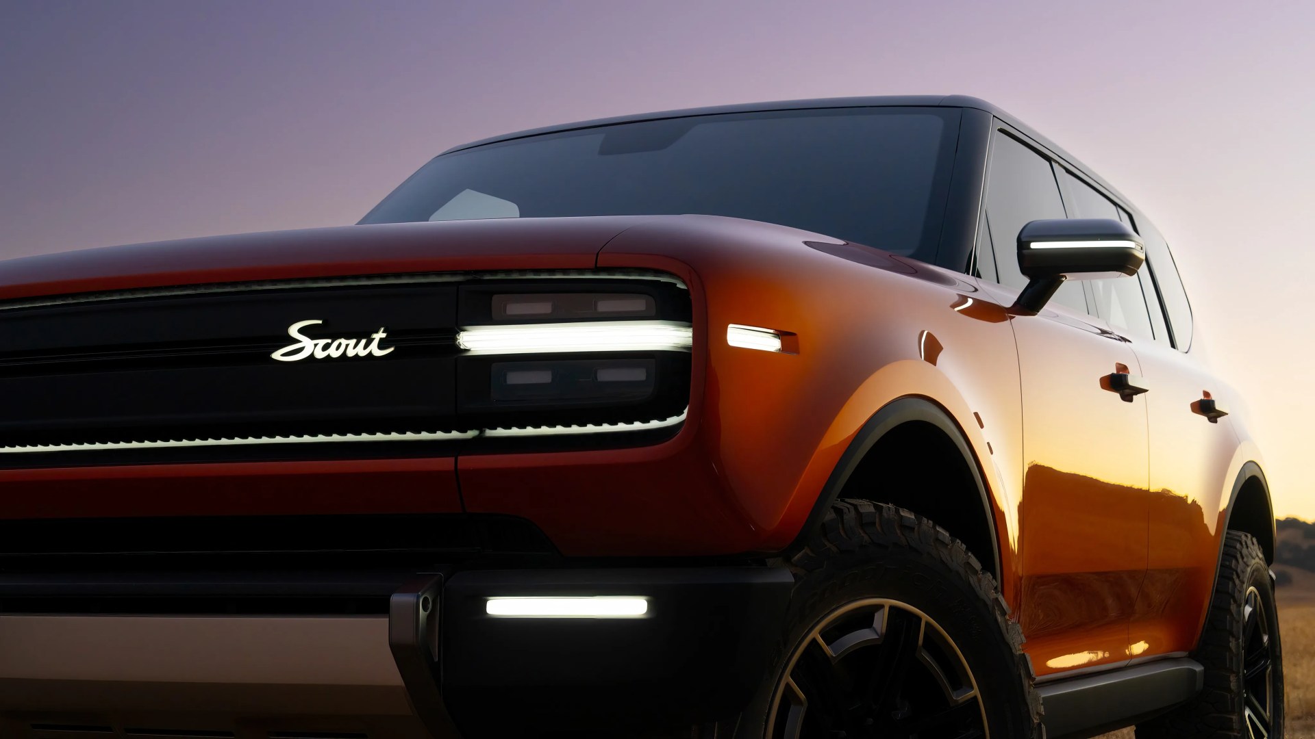 Orange Scout SUV with illuminated front grille and headlights at dusk.