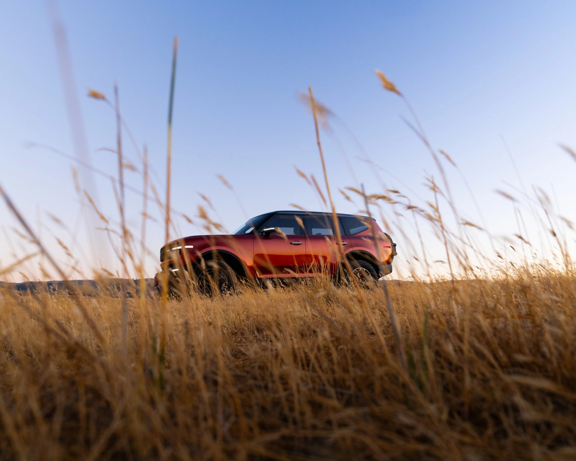 Red SUV with black roof parked in a dry grassy field under a clear blue sky.