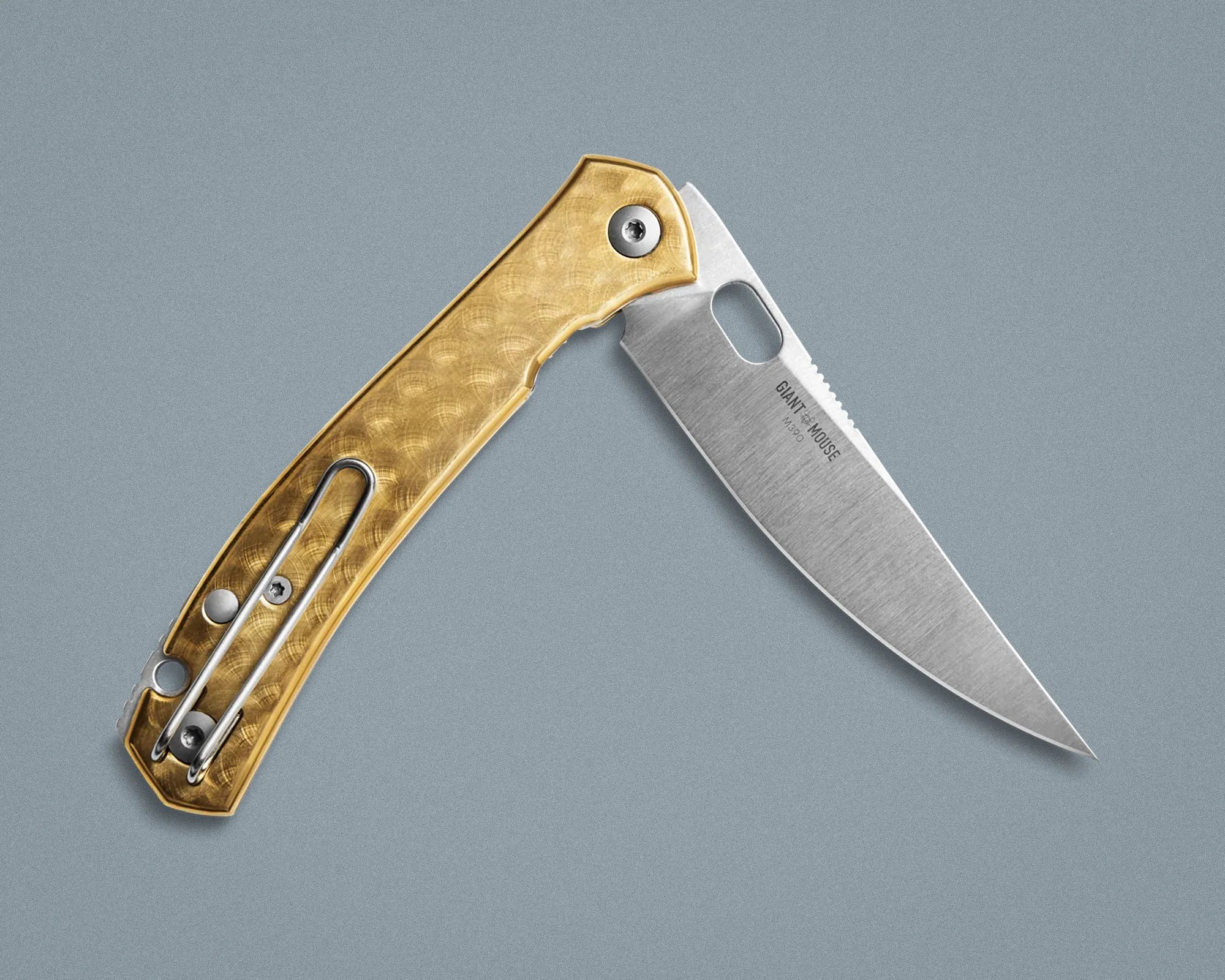 Folding pocket knife with a textured gold handle and a partially serrated stainless steel blade on a gray surface.