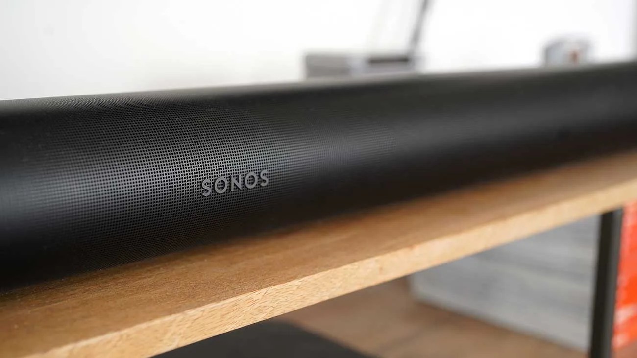 Black Sonos soundbar with perforated grille on a wooden shelf.