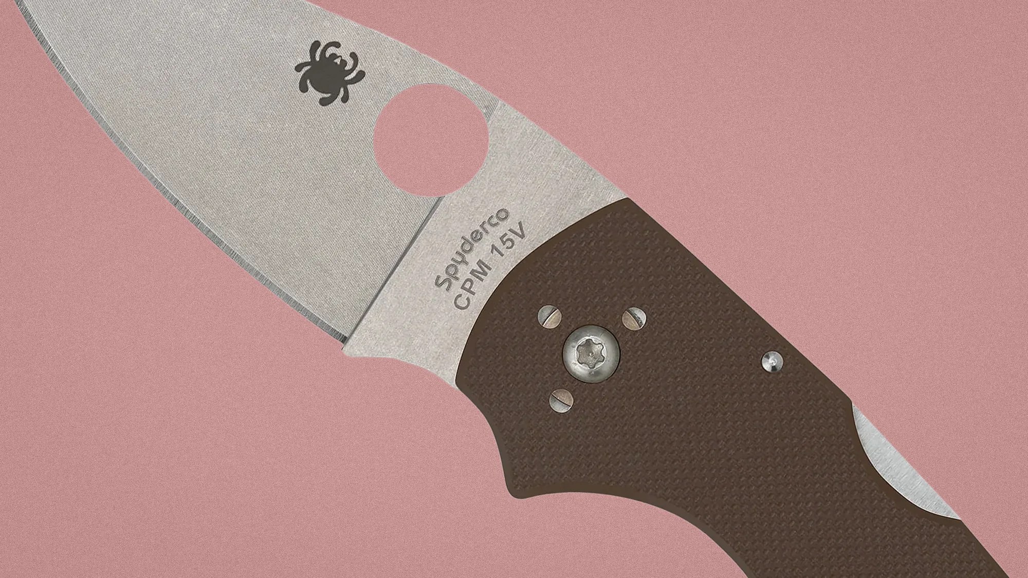 Close-up of a Spyderco CPM 15V folding knife blade with a brown textured handle on a pink background.