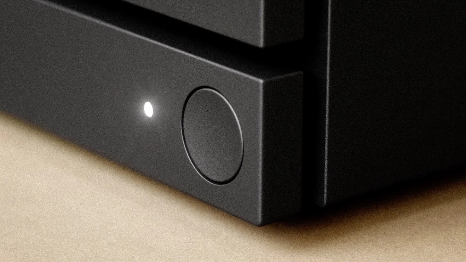 Close-up of a black electronic device corner with a round button and a small illuminated white LED light.