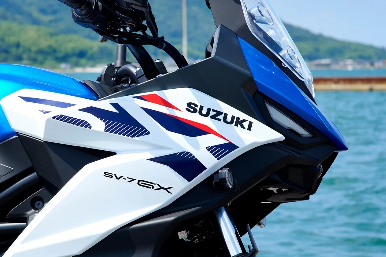 Close-up of a blue, white, and black Suzuki SV-7 GX motorcycle front fairing with red and navy graphics by the water.