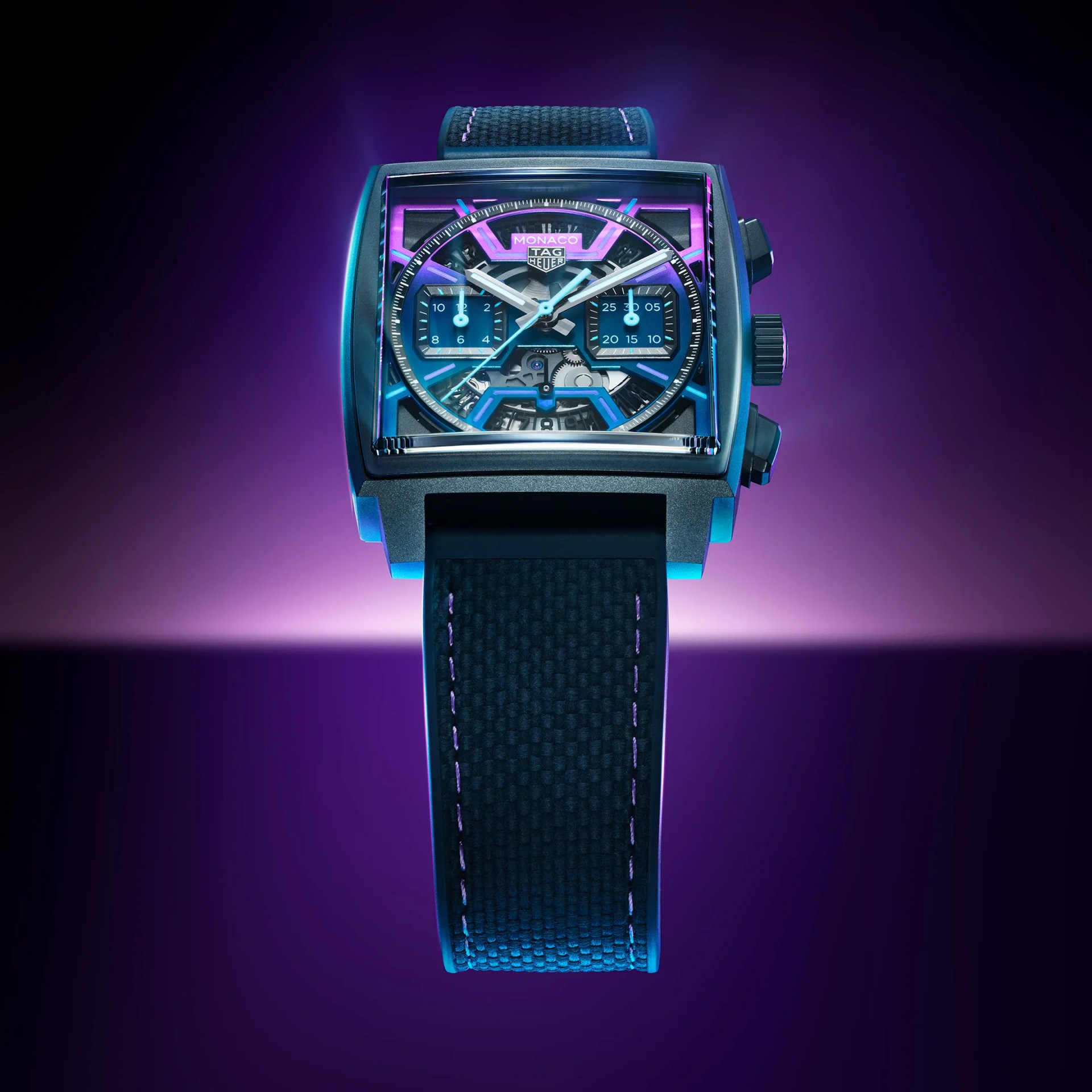 Square TAG Heuer Monaco watch with black textured strap and neon blue and purple accents on the dial.