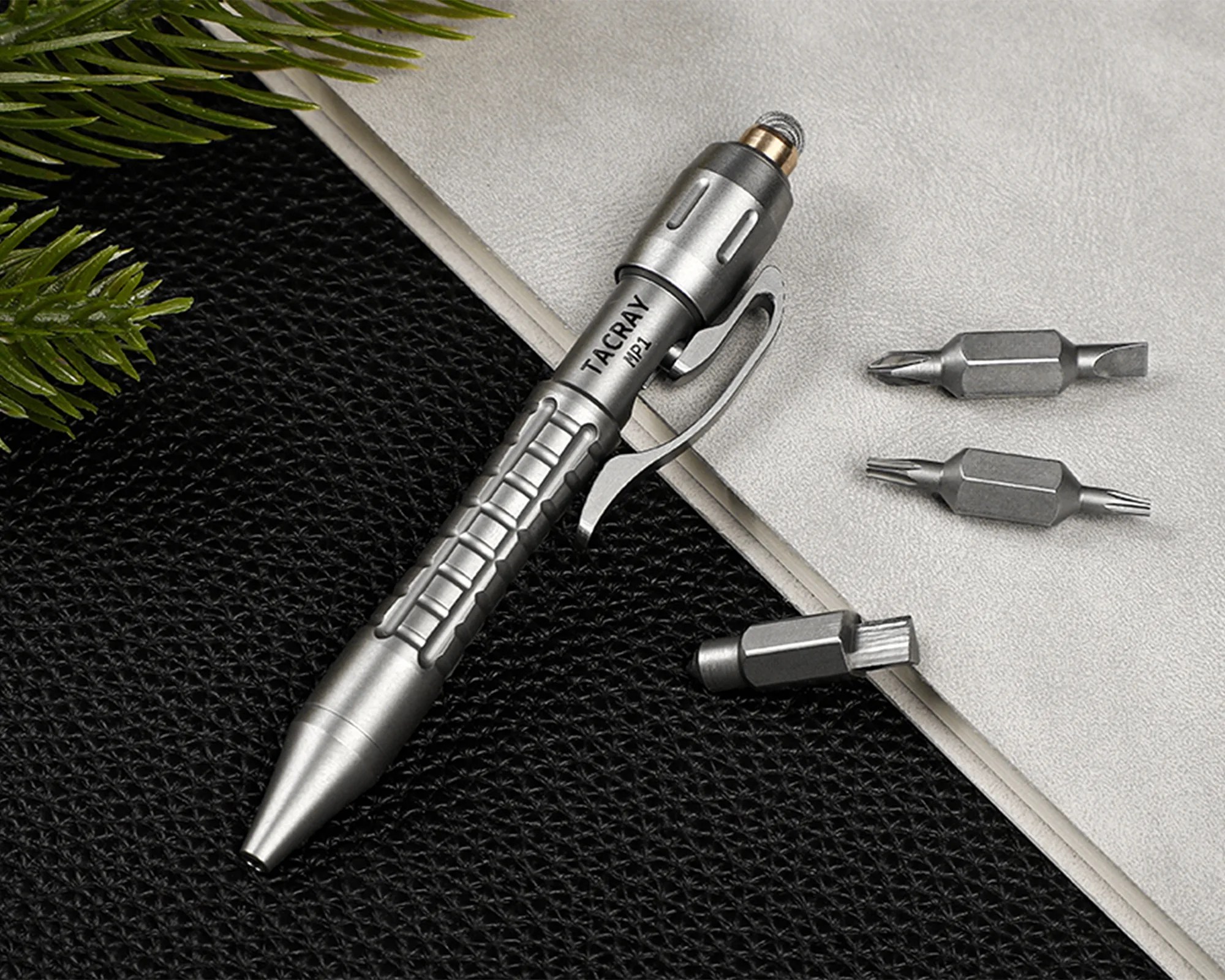 Silver multi-bit screwdriver pen with textured grip and three interchangeable bits on a black and gray surface.